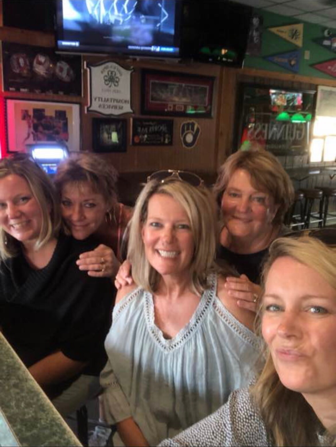 Five women smiling and posing for a selfie at a bar or pub.”,
