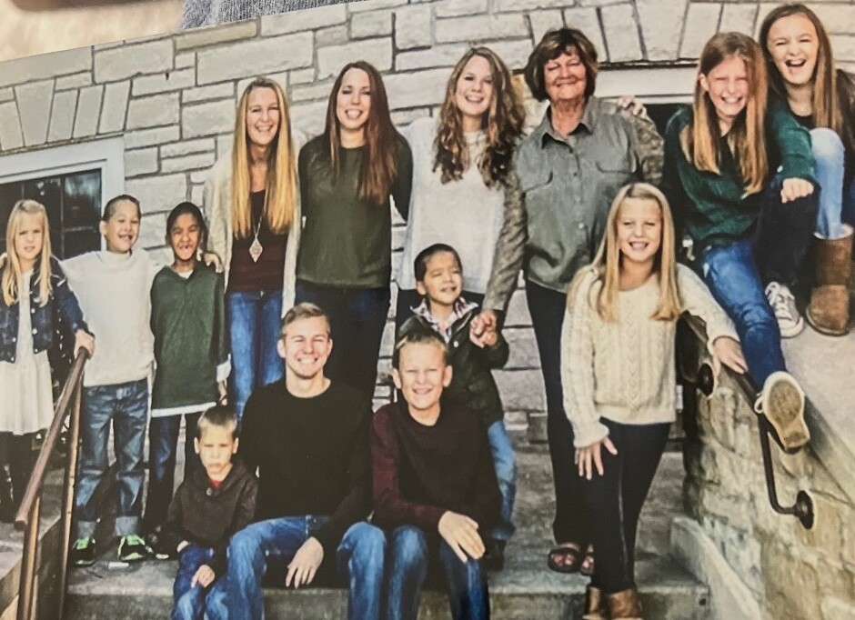 Group of smiling kids and two adults posing on stone steps outdoors.