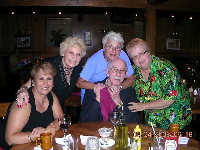 Five older adults posing together at a restaurant table, smiling for the camera; glasses and a bottle on the table and a date stamp reading 06-24-2008.