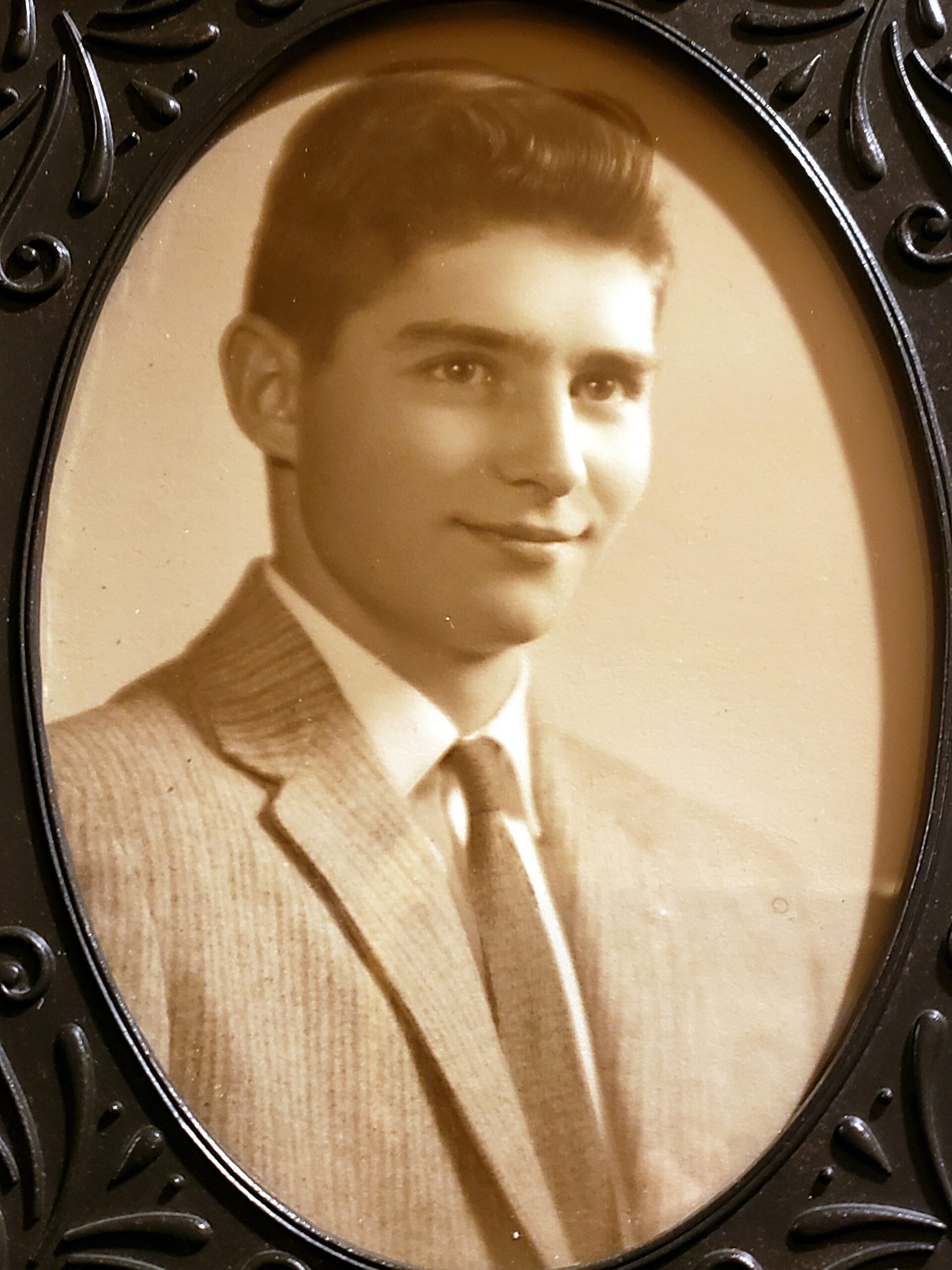 Sepia-toned portrait of a young man in a suit and tie, mounted in an ornate oval frame.