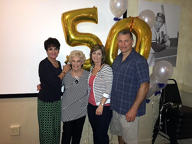 Four adults posing together at a 50th‑birthday party, with large gold '50' balloons in the background and other balloons visible nearby.