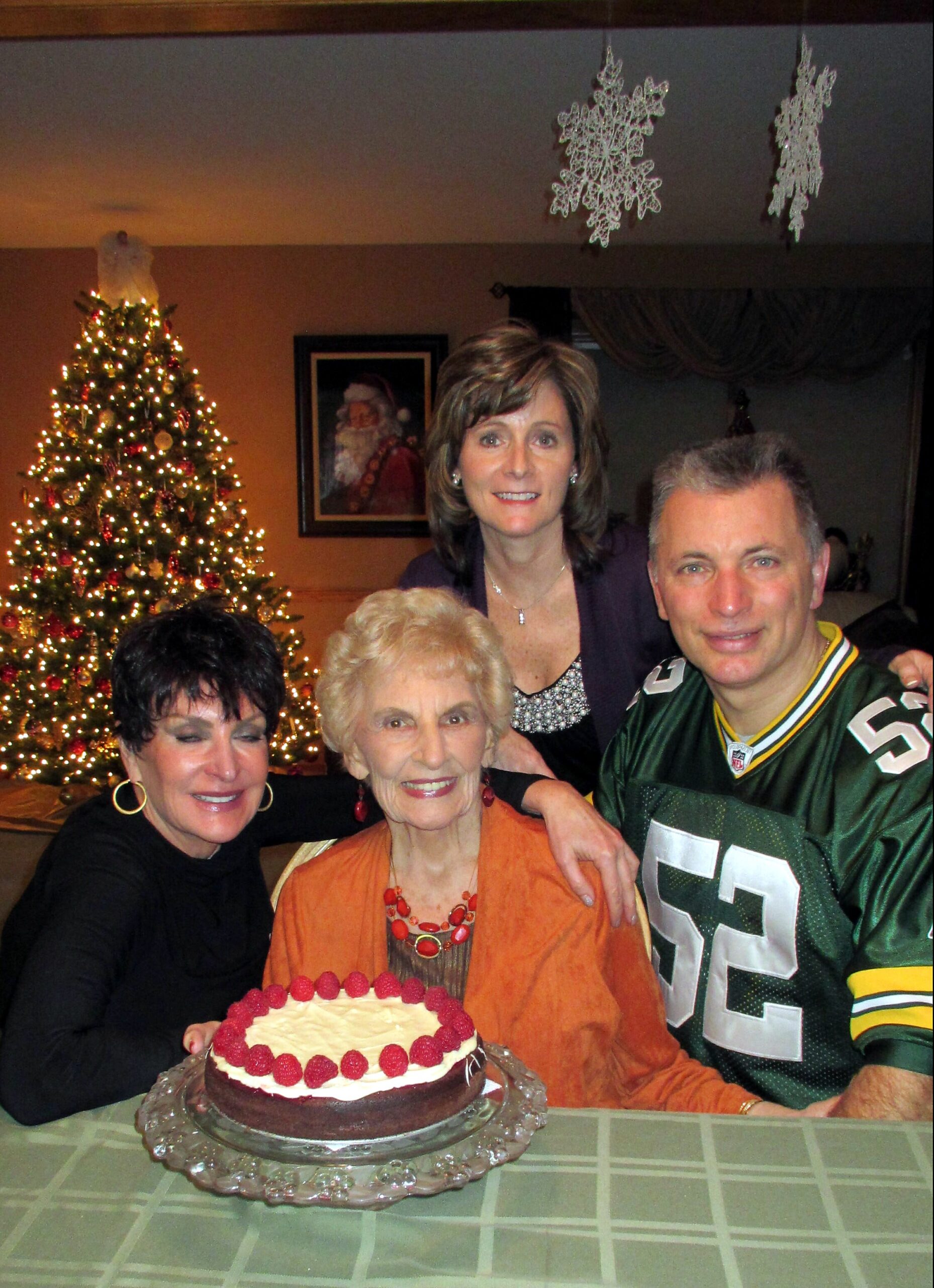 Group of relatives celebrating Christmas with a cake in front of a decorated tree and shows a warm family gathering scene at home.