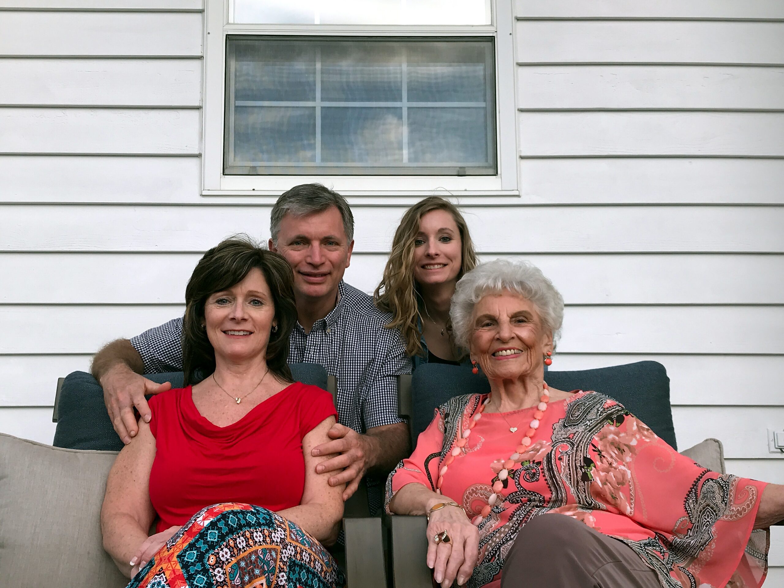 Family of five posing together on a porch with white siding in the background, all smiling at the camera.