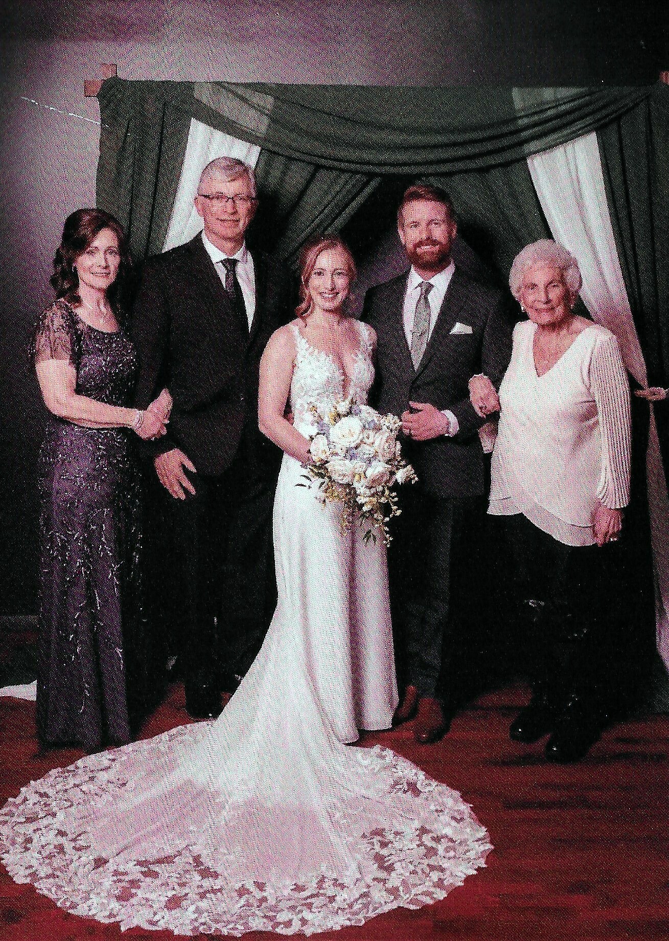 Bride in a white gown holding a bouquet, flanked by the groom and two guests in formal attire.