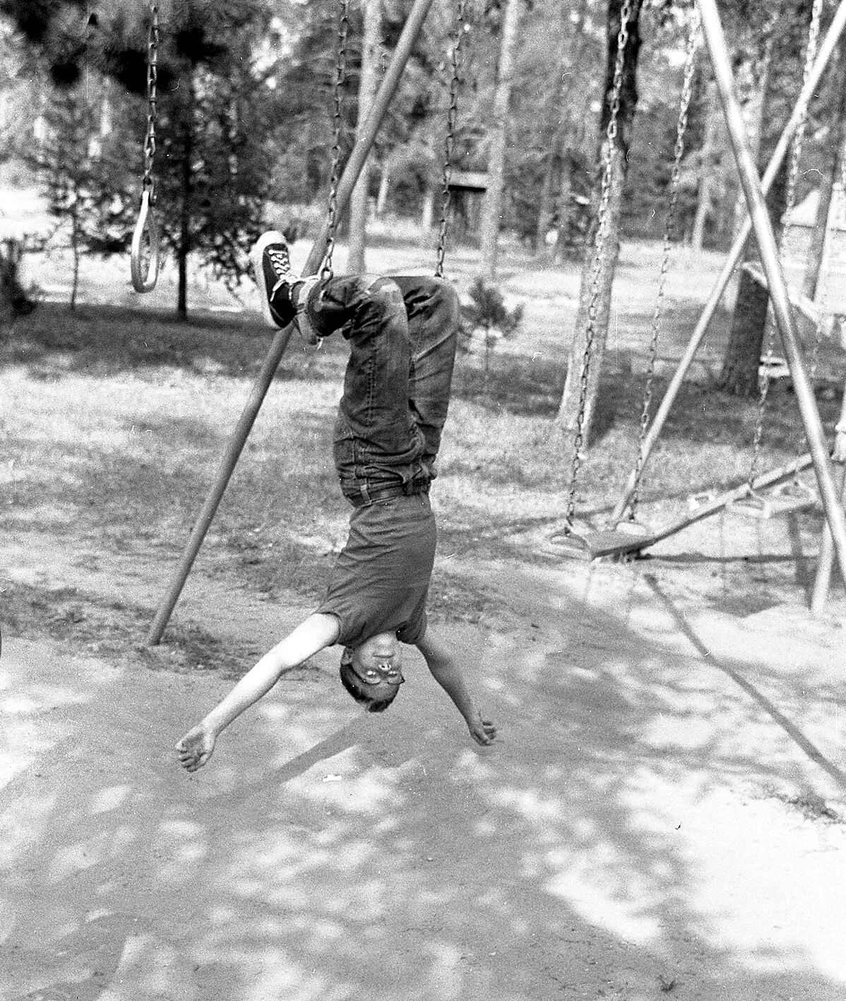 Child upside down on a swing in a park, arms extended as they hang from the seat.
