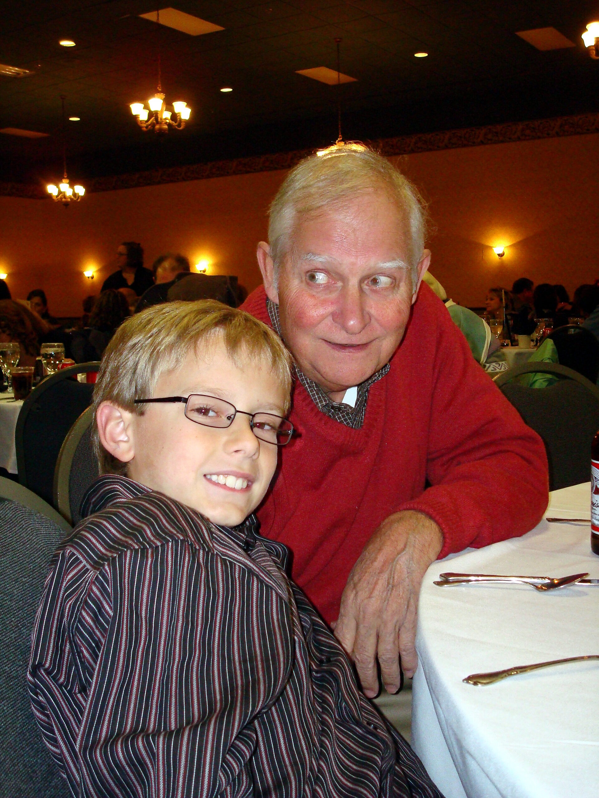 Grandfather and grandson posing at a banquet table in a dimly lit restaurant.