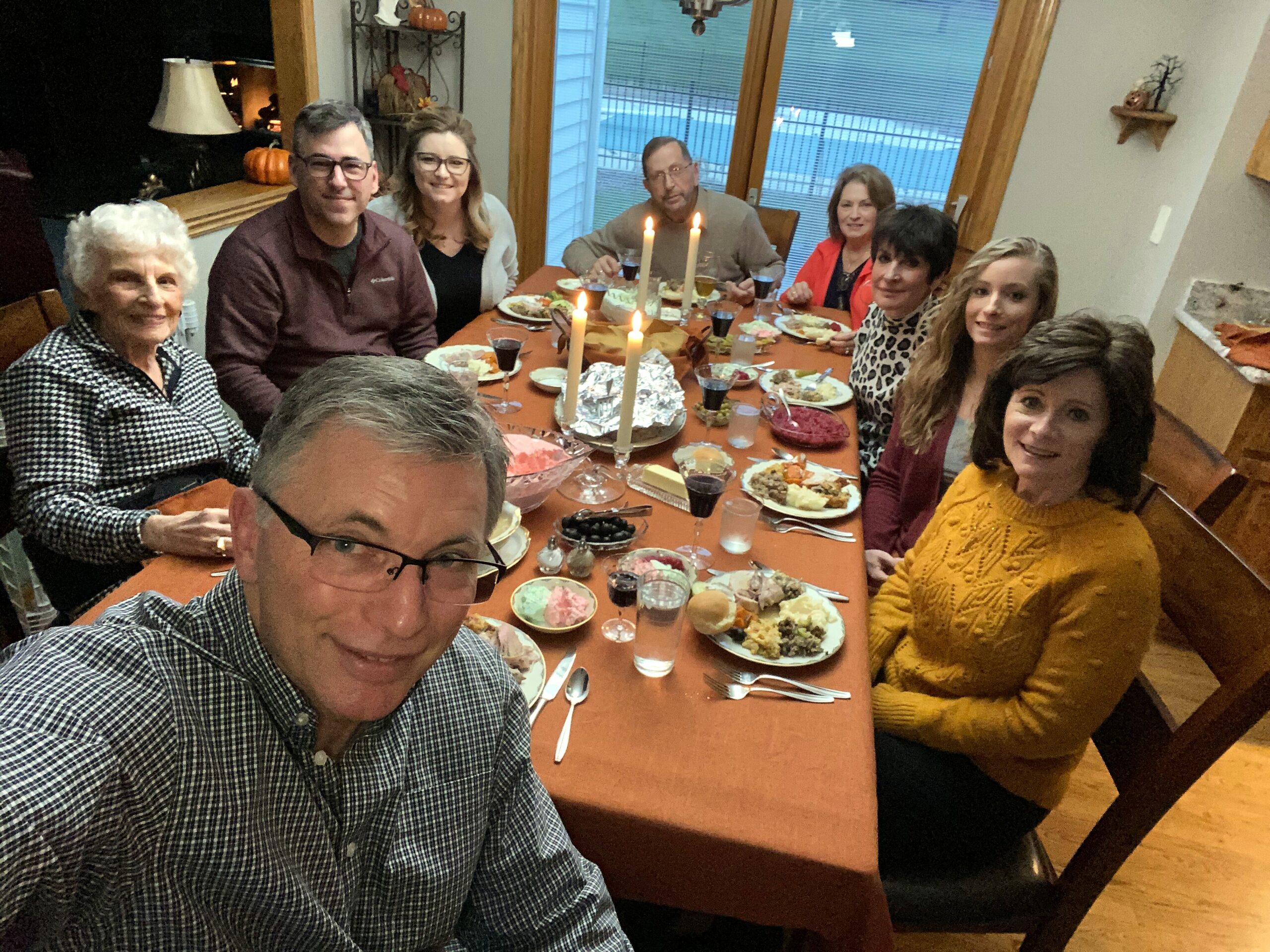 A group of adults smiling at a dinner table with candles, sharing a home-cooked meal indoors.