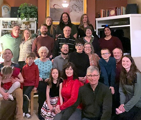Large multi-generational group of family and friends posing for a photo in a living room, all smiling.