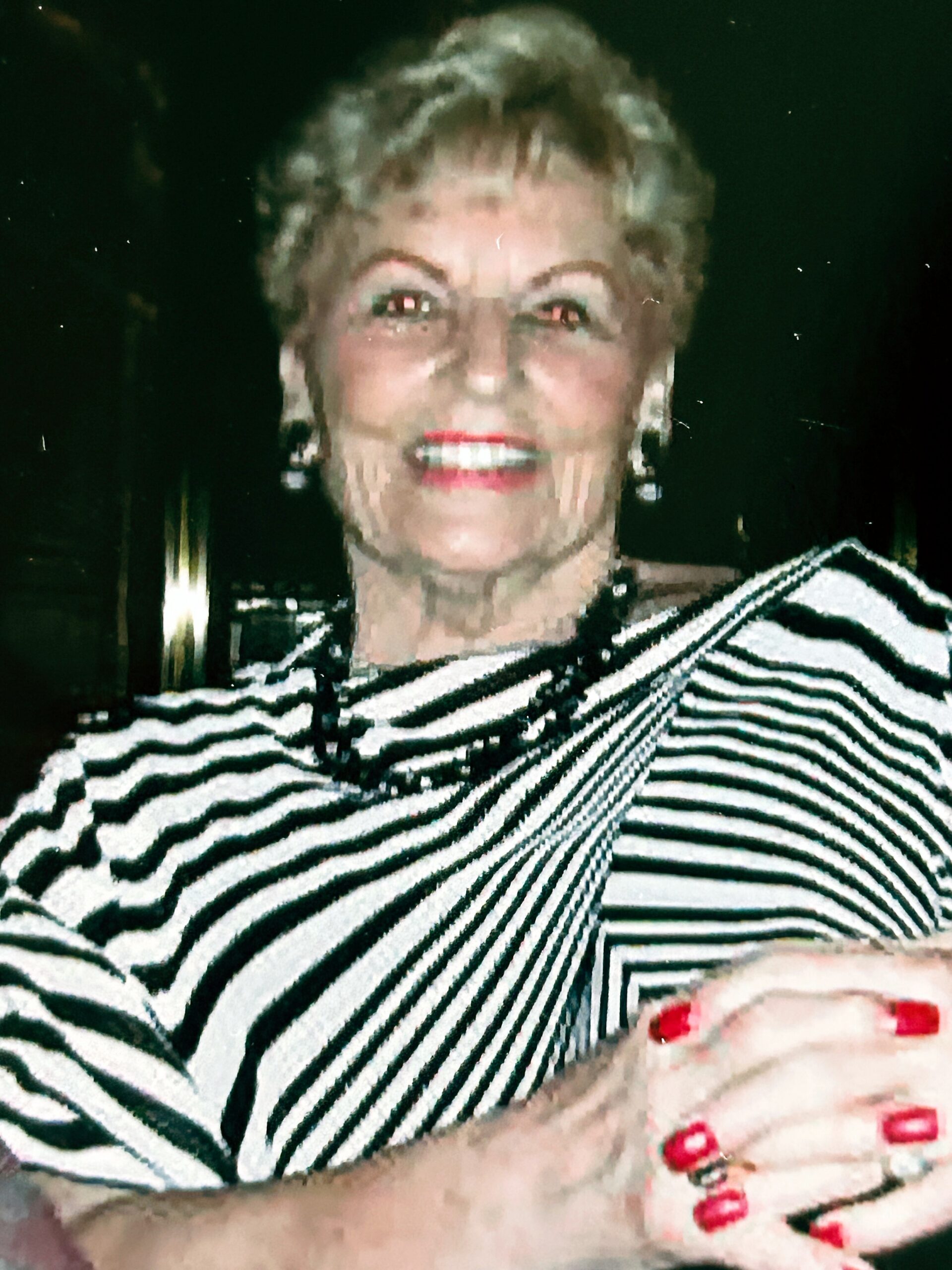 Close-up portrait of a smiling woman with short blond hair, wearing a black-and-white striped top, against a dark background.