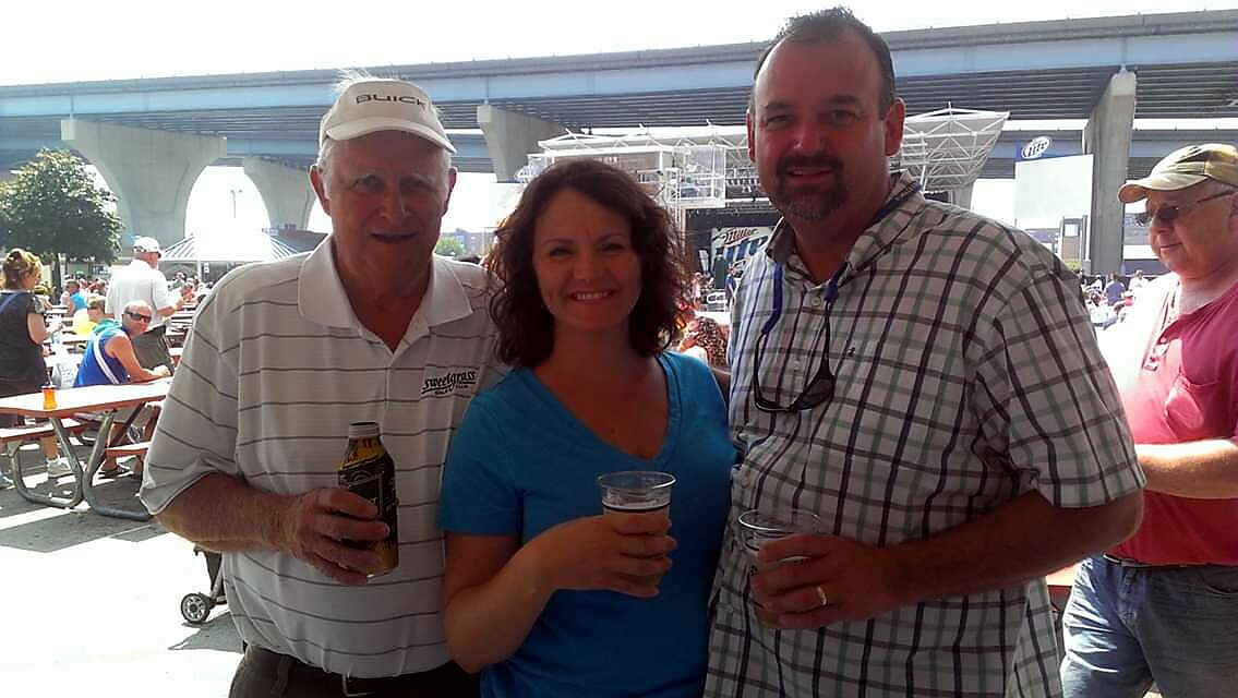 Three adults posing at an outdoor festival, each holding a drink and smiling.