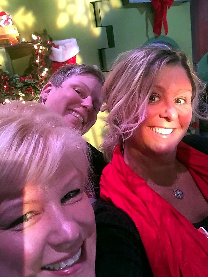 Three adults posing for a cheerful holiday selfie with Christmas decorations in the background on a festive set.