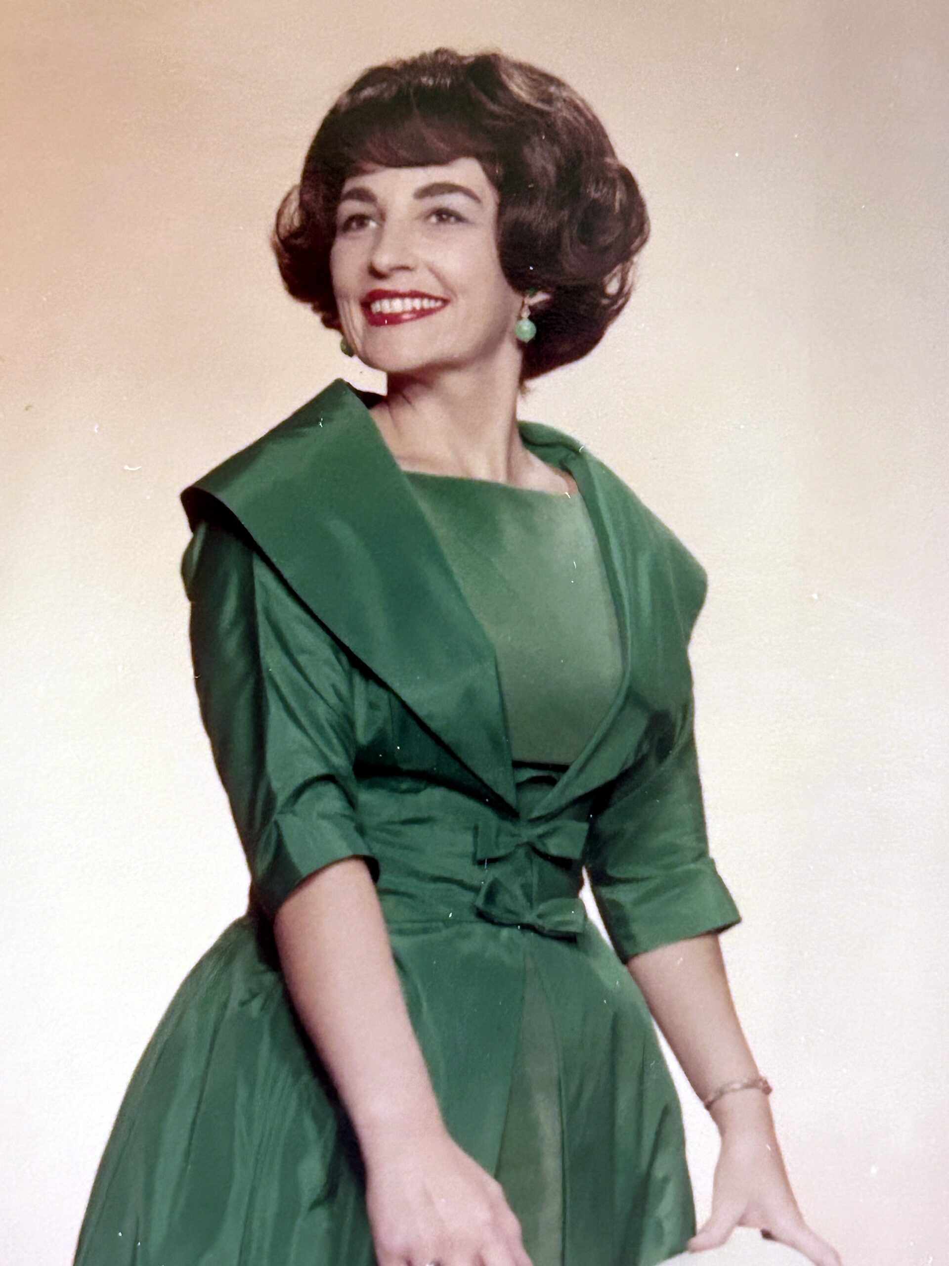 Smiling woman in a green vintage dress, posing against a neutral backdrop.