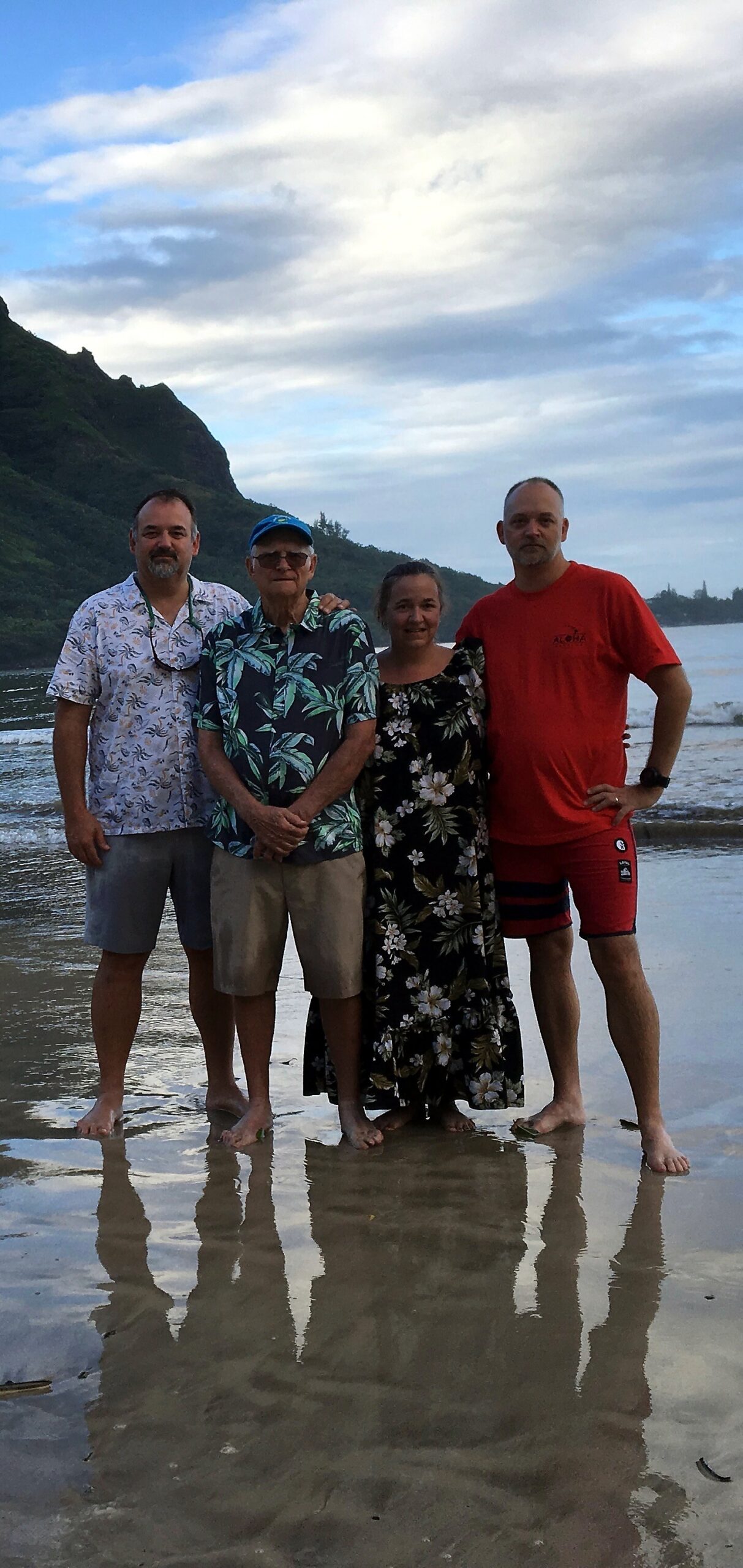 Group of four adults standing on a wet beach with mountains and cloudy sky in the background.