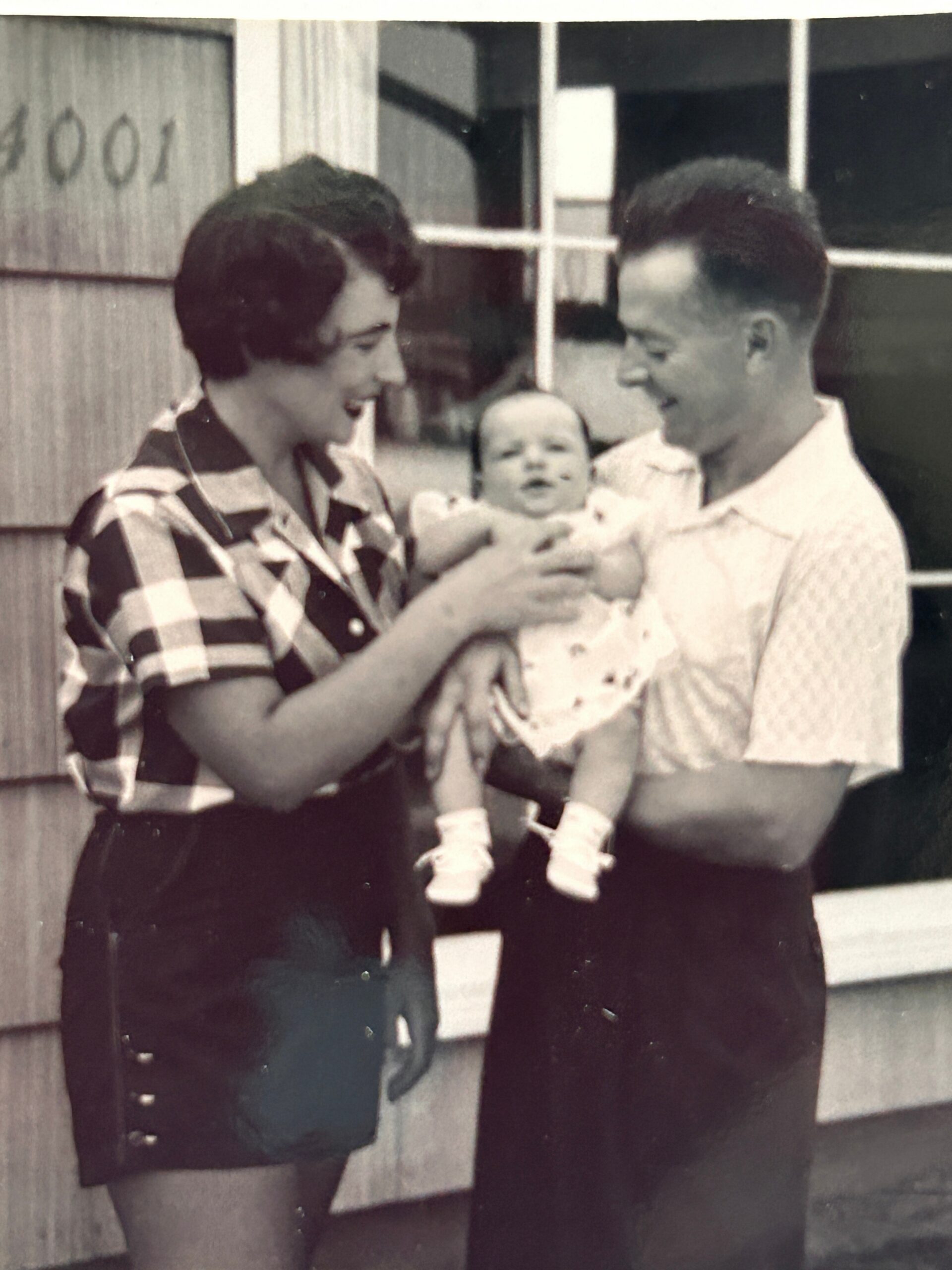 Couple smiling as they hold a baby outdoors in a black-and-white photo.