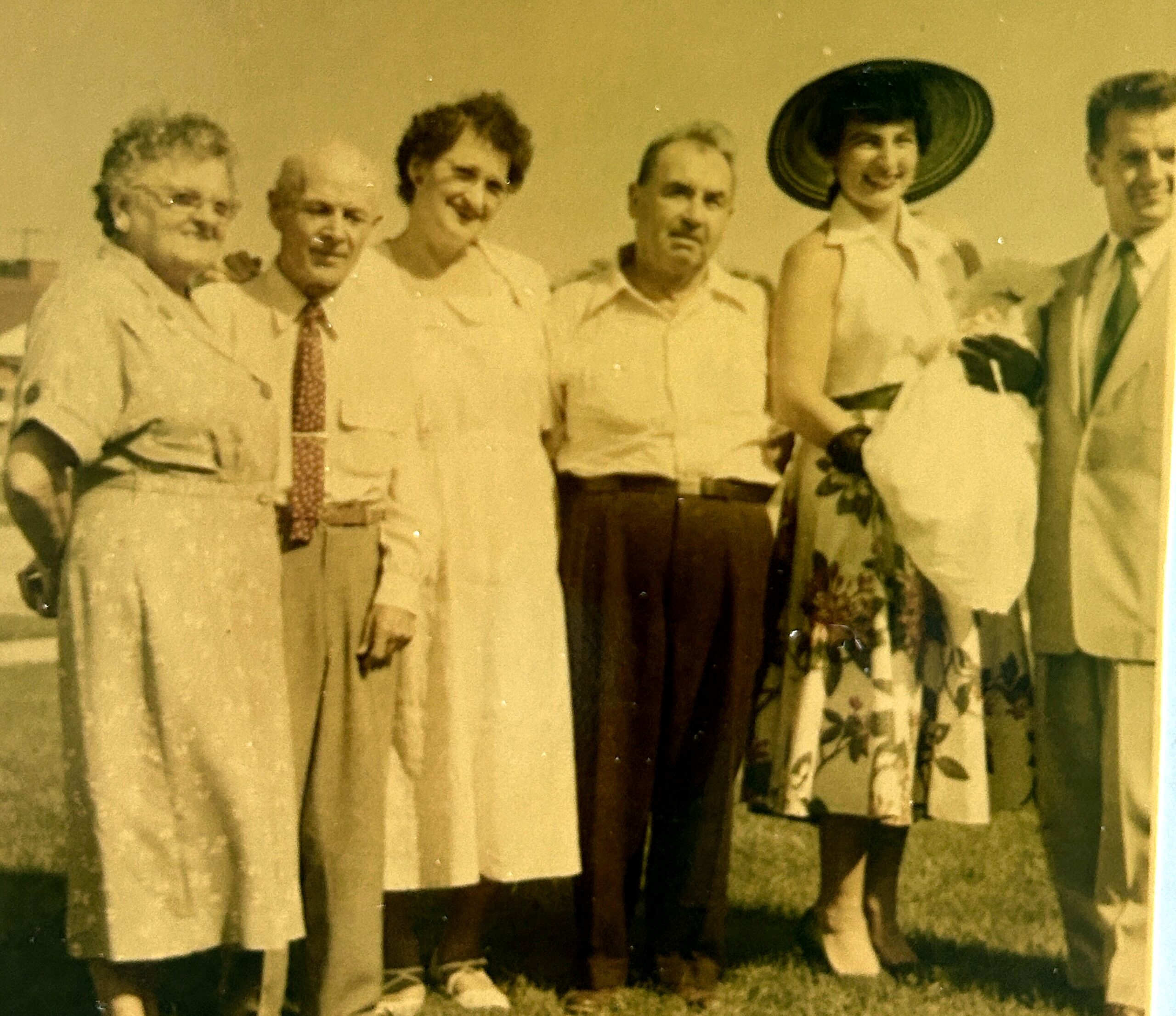 Sepia-toned group portrait of adults standing outdoors, dressed in mid-20th-century clothing, posing for the photo.