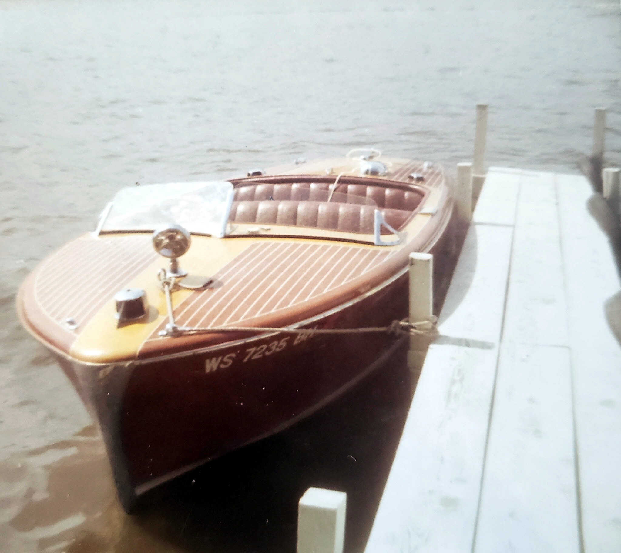 Wooden motorboat with a varnished deck moored at a wooden dock on calm water, hull marked WS-7235.