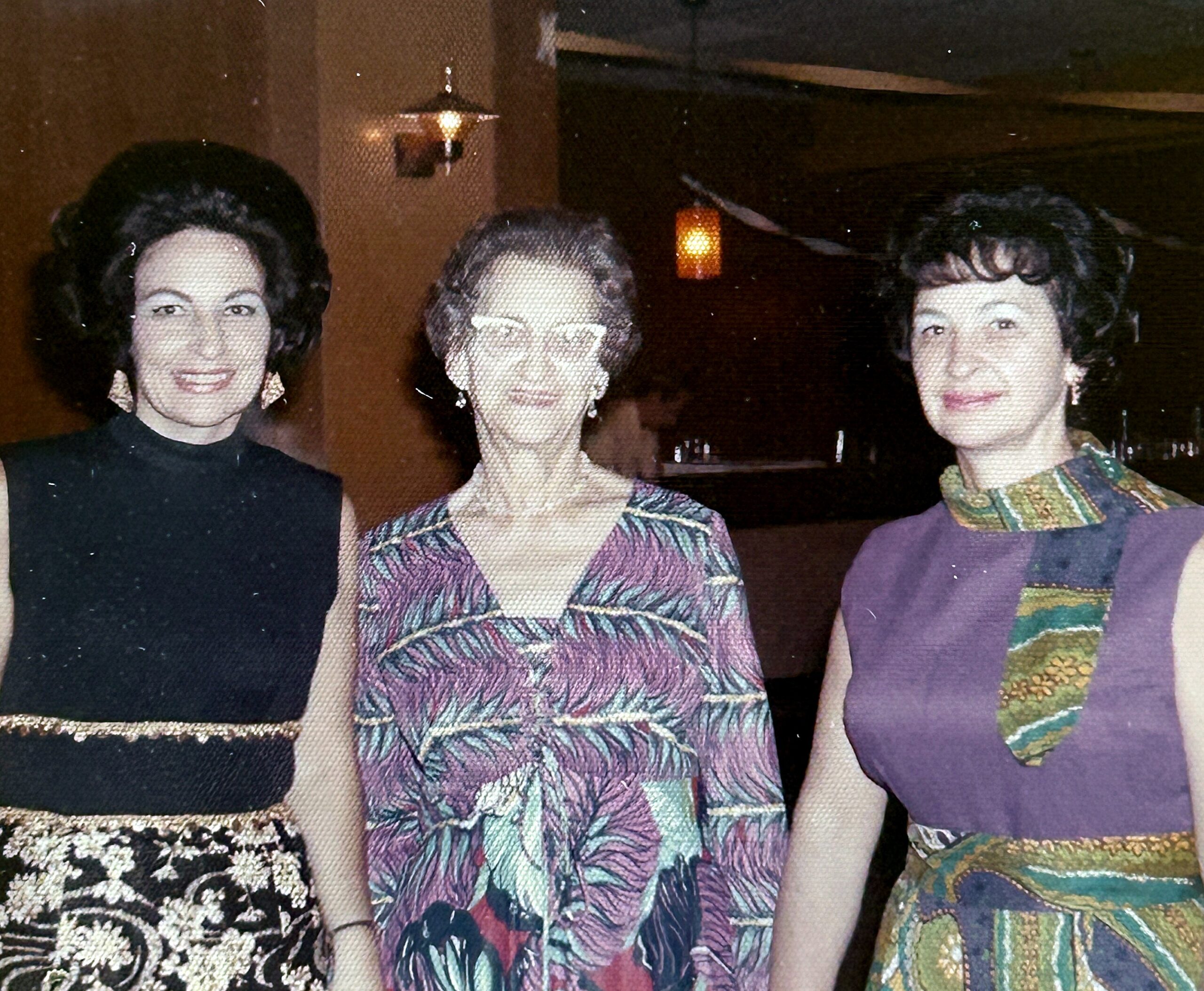 Three women in formal dresses posing together for a group photo at a social event.”,
