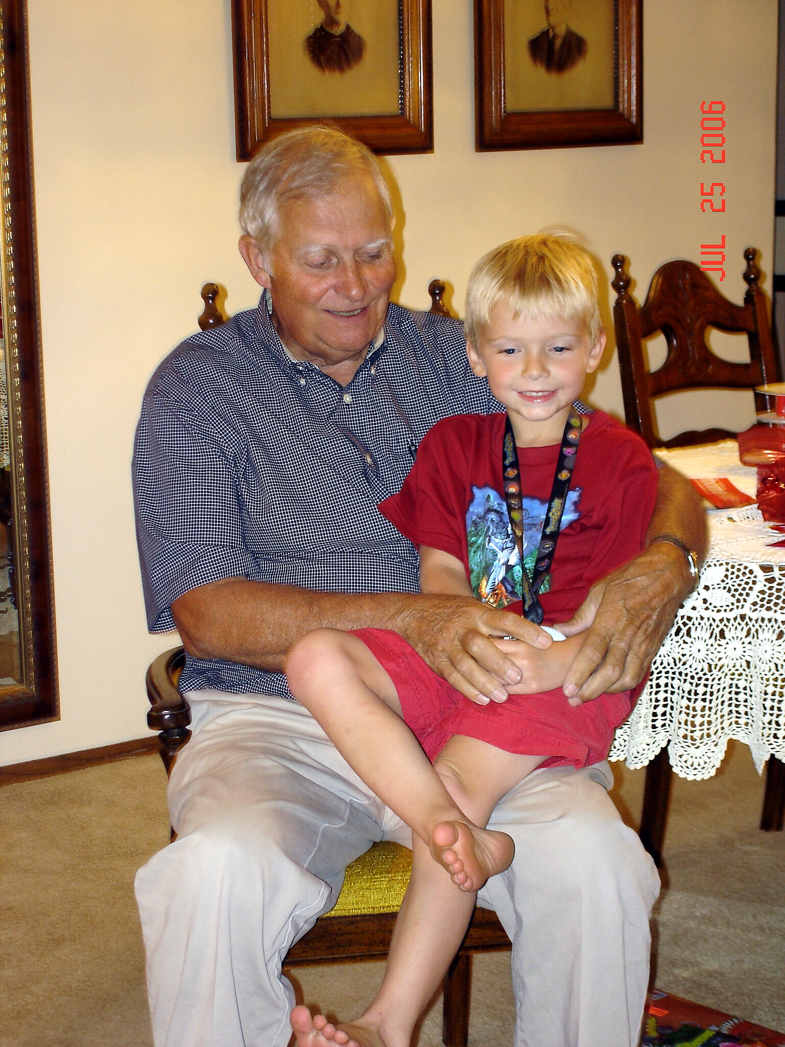 Grandfather and young boy sitting together on a chair indoors, smiling at the camera.
