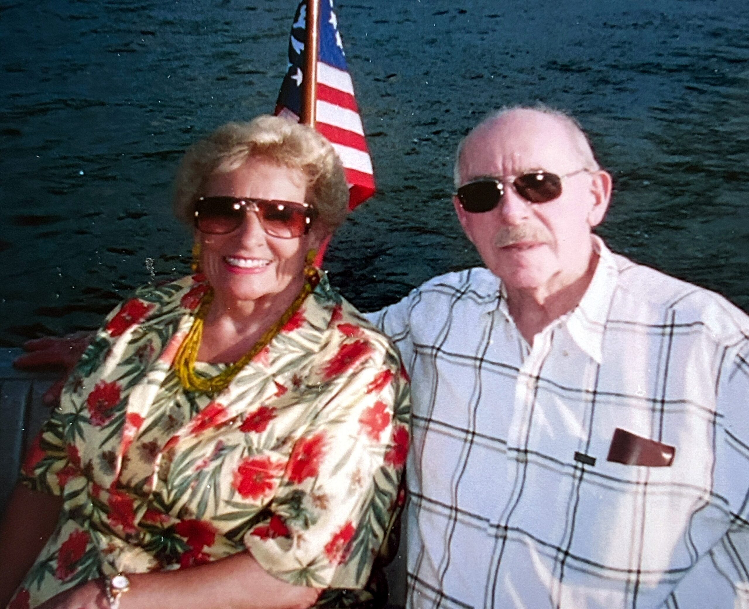 Older couple posing for a photo on a boat with an American flag in the background.