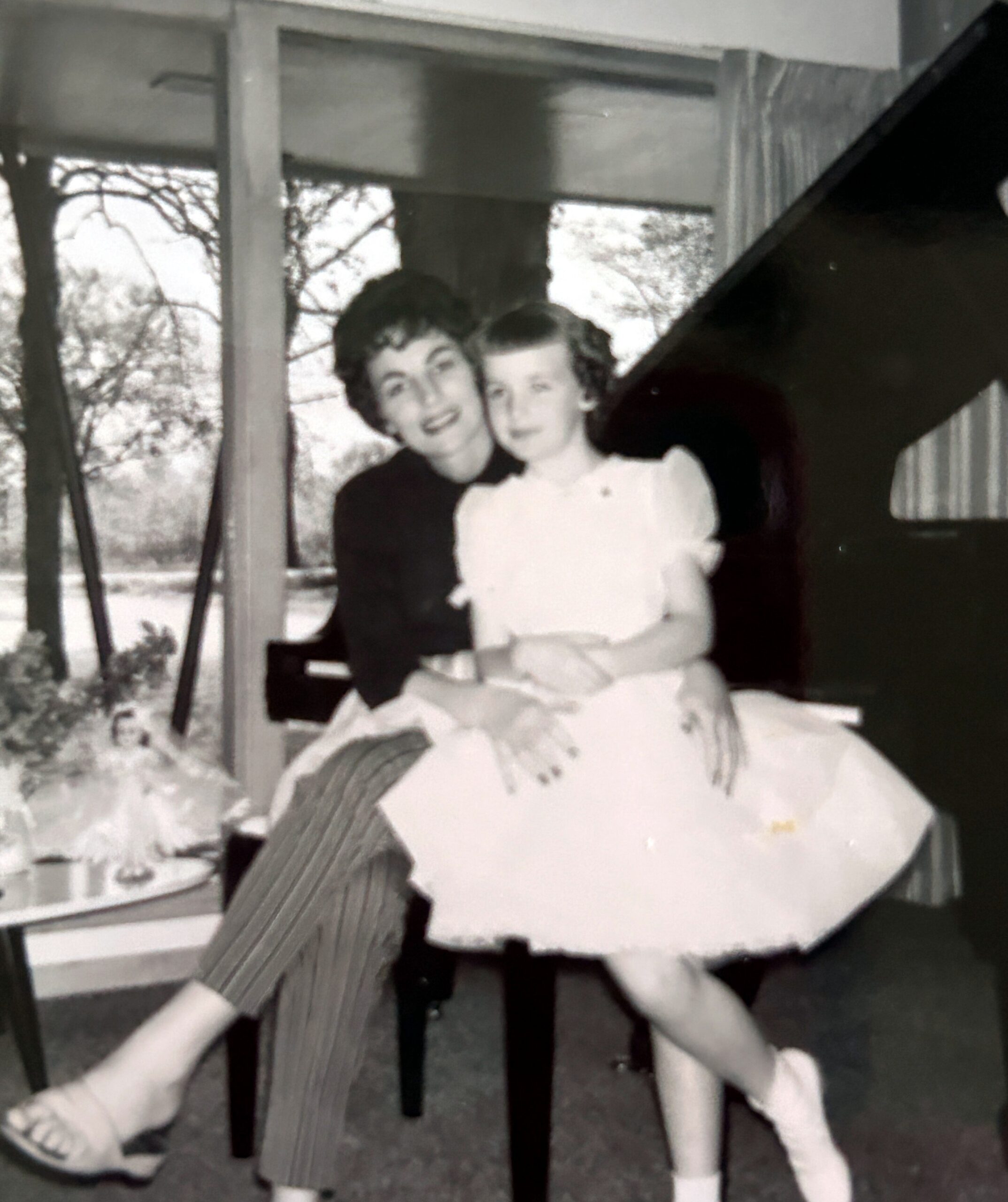 Mother and daughter sitting together indoors, smiling for a formal photo in a vintage setting.