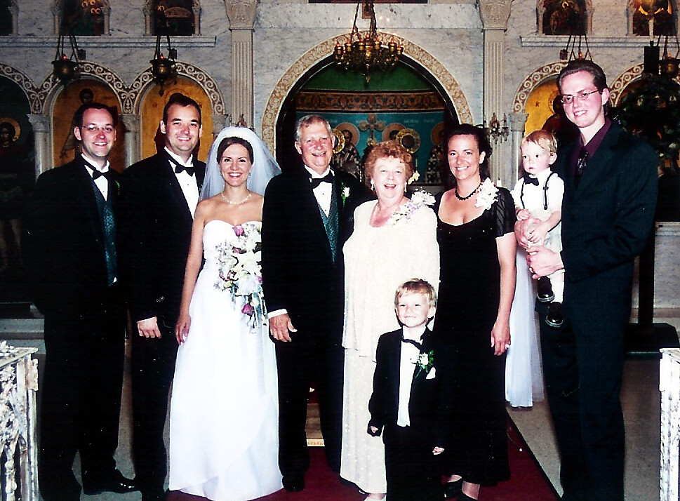 Bride in a white gown and groom in a tuxedo stand with family inside an ornate church for a wedding.