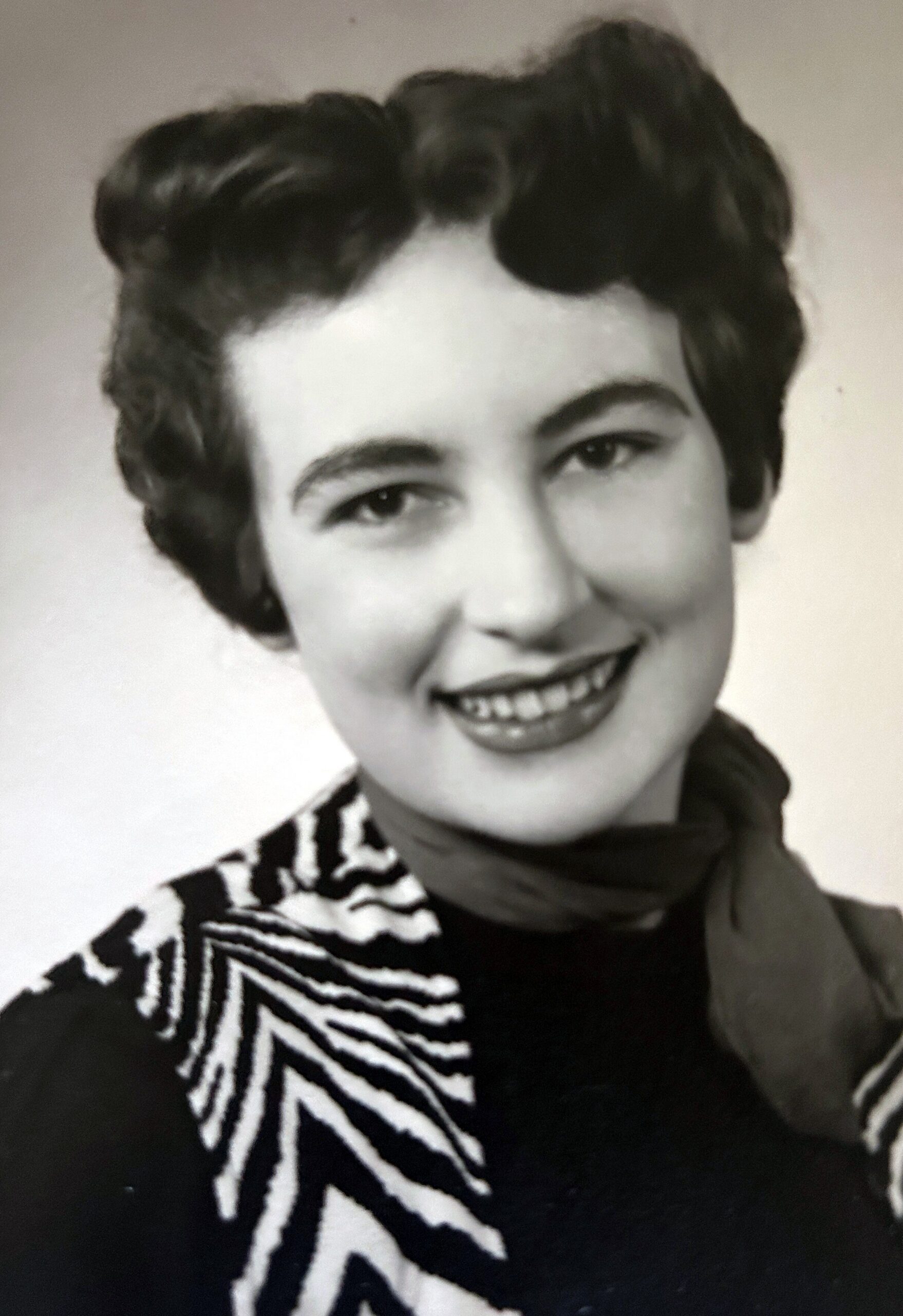 Black-and-white portrait of a smiling person with short dark hair wearing a zebra-patterned sweater and scarf.