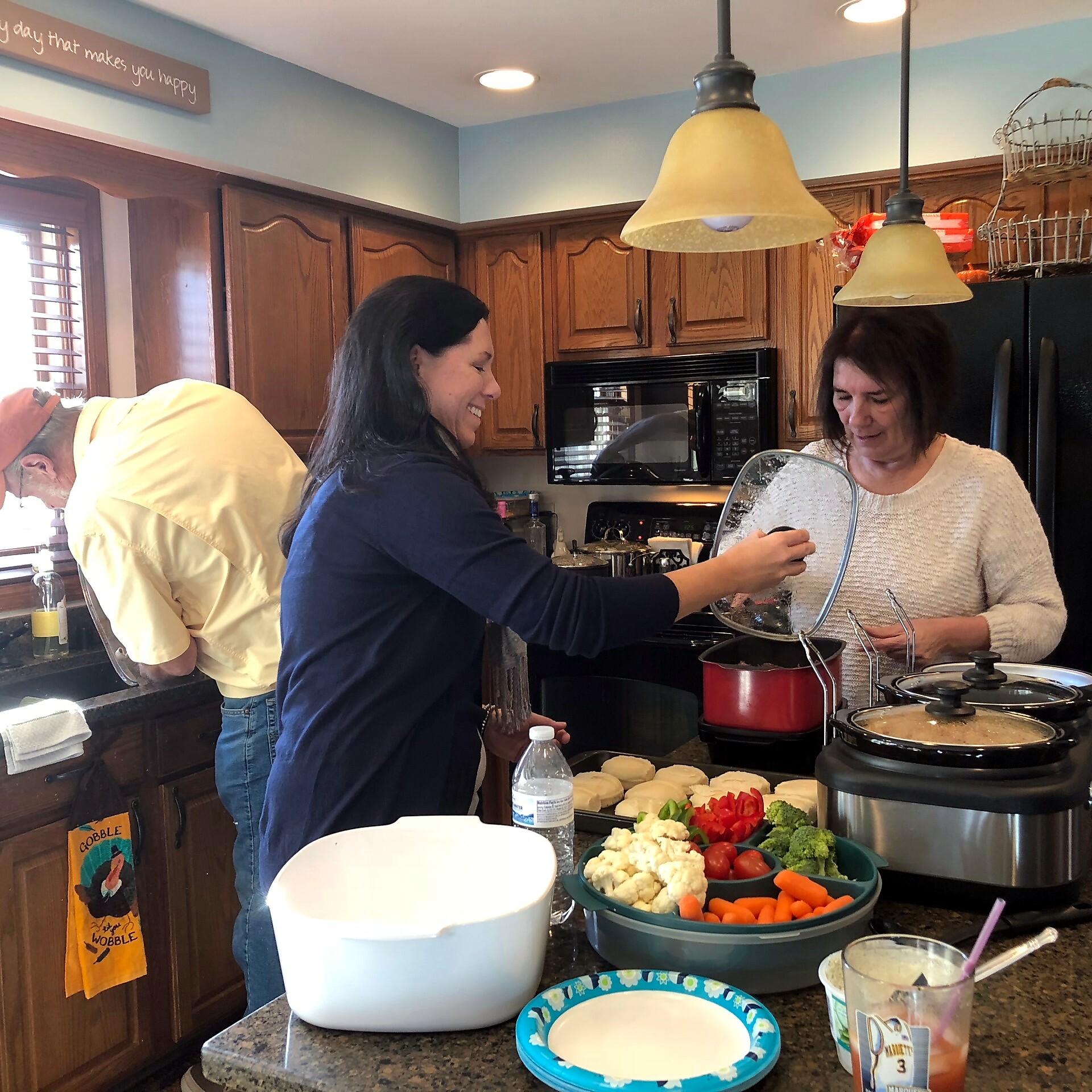 Two women cooking in a home kitchen, with bowls of chopped vegetables and a red pot on the stove nearby.