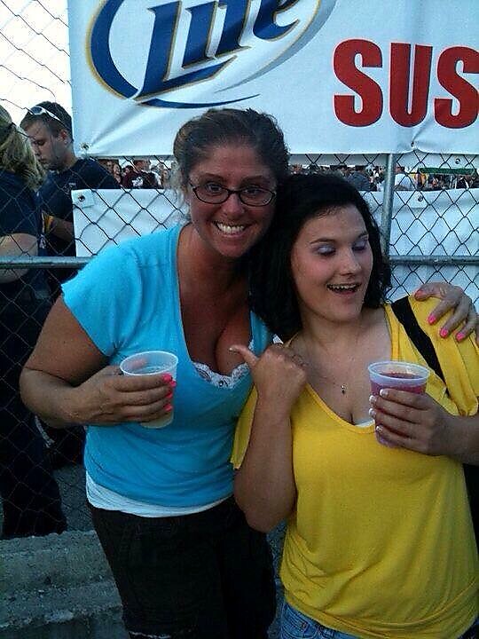 Two smiling women posing together at an outdoor event, each holding a plastic cup.