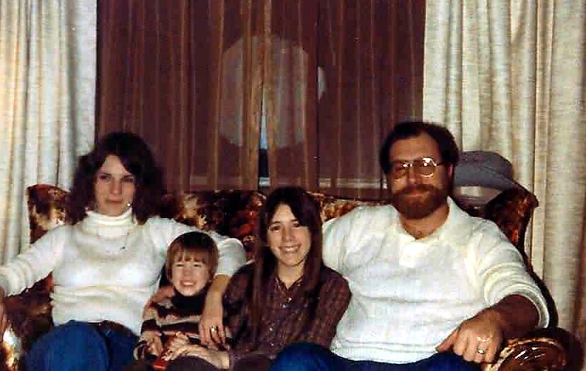 Family of four sitting on a floral sofa in a living room, smiling at the camera.
