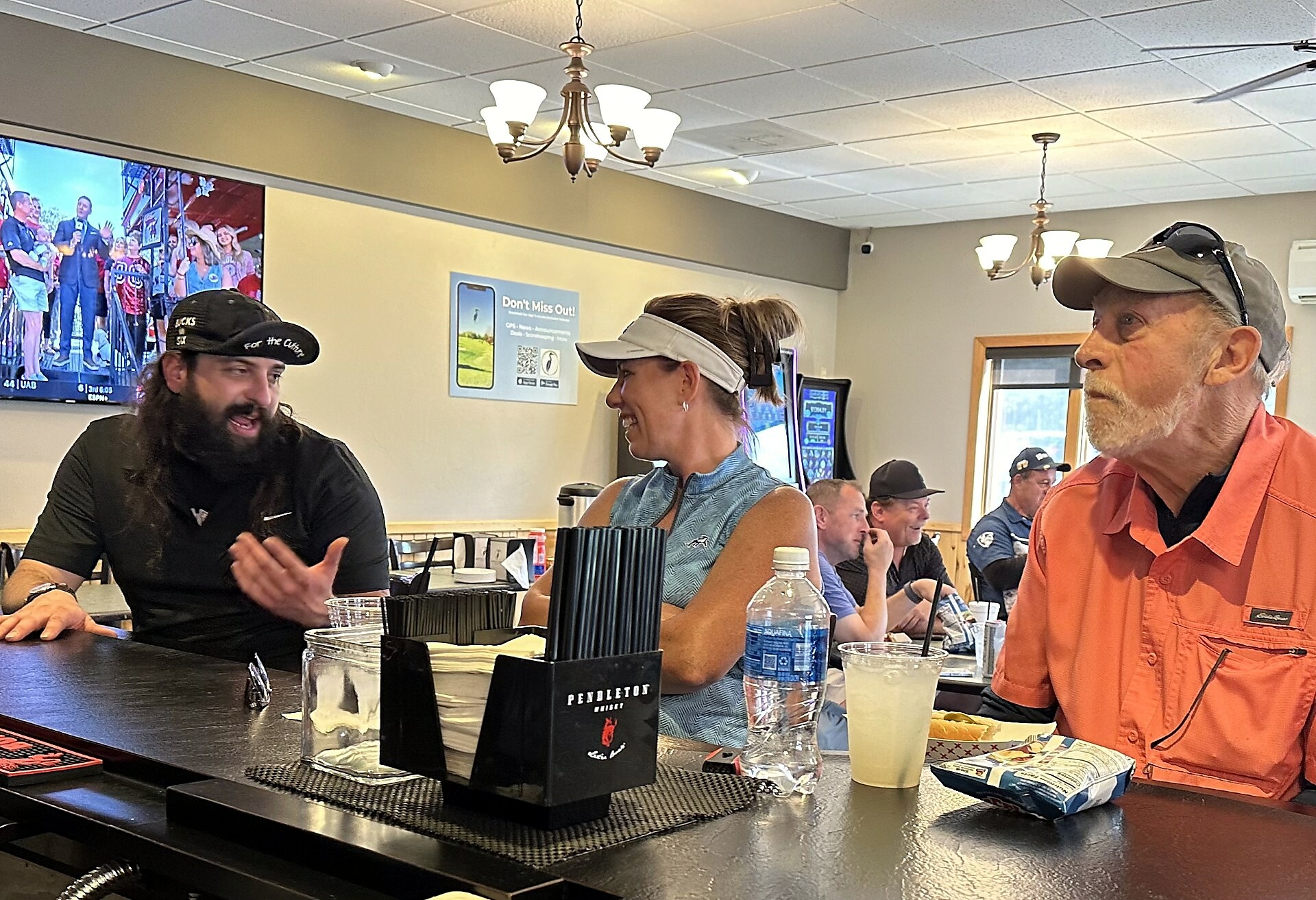 People sit at a bar counter in a casual cafe, chatting and smiling at each other while drinks sit in front of them.