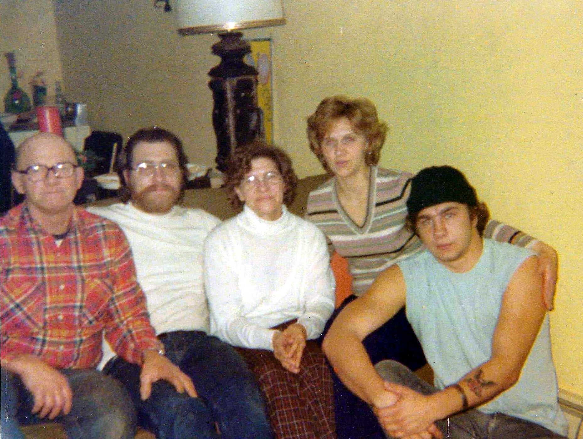 Five people sit closely together on a couch in a living room, posing for a photo and smiling at the camera.