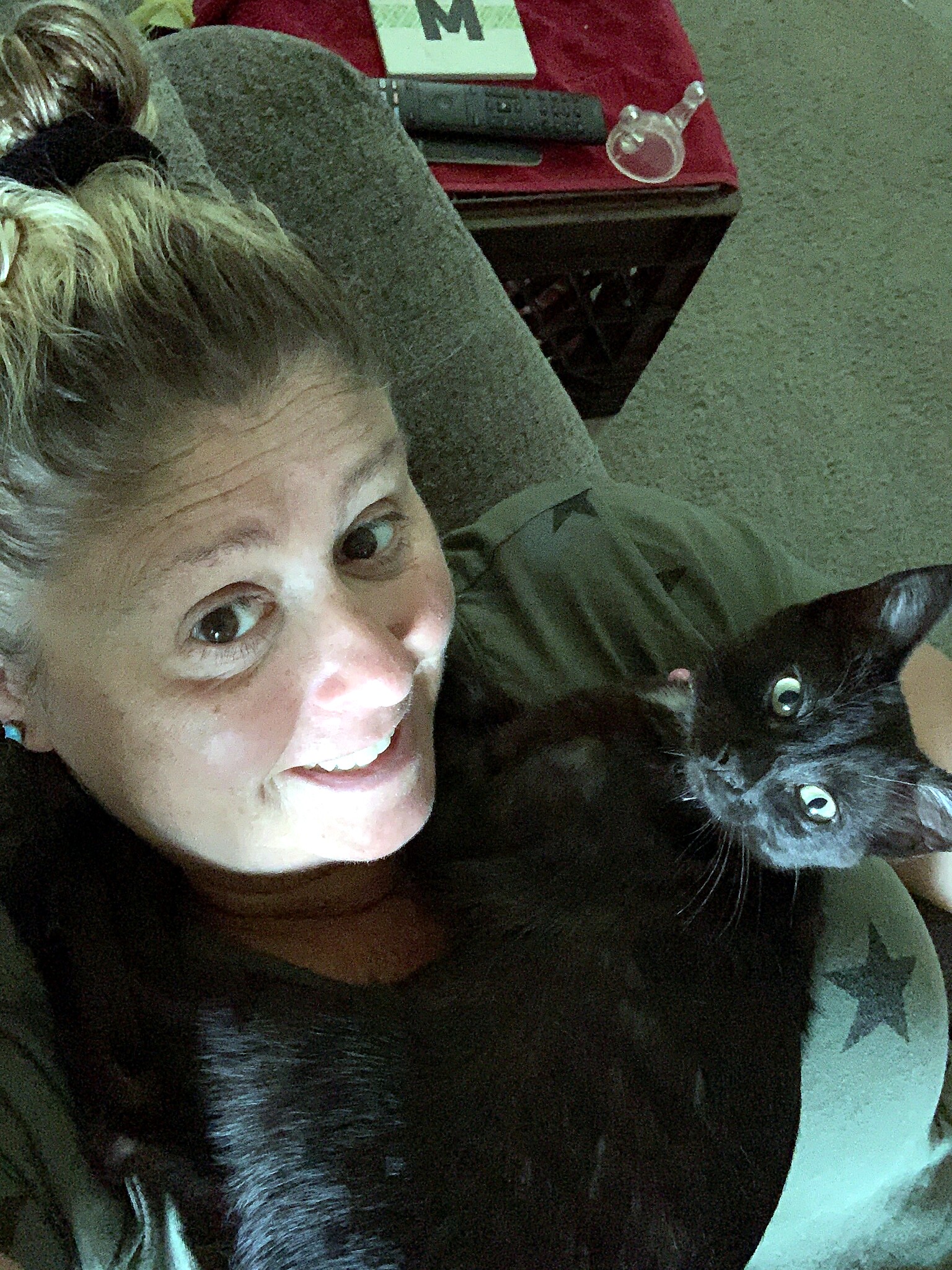 Smiling woman lying down next to a black cat, both looking at the camera.