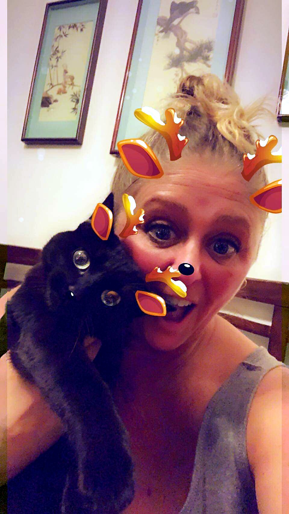 Woman with a black dog close to her face, wearing a playful deer filter with antlers and nose.
