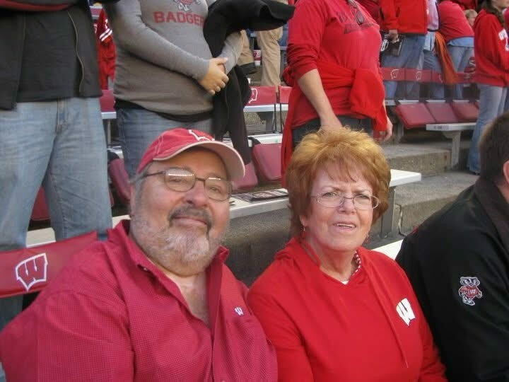 Smiling couple in red at a sports stadium, seats and fans in red around them in the stands