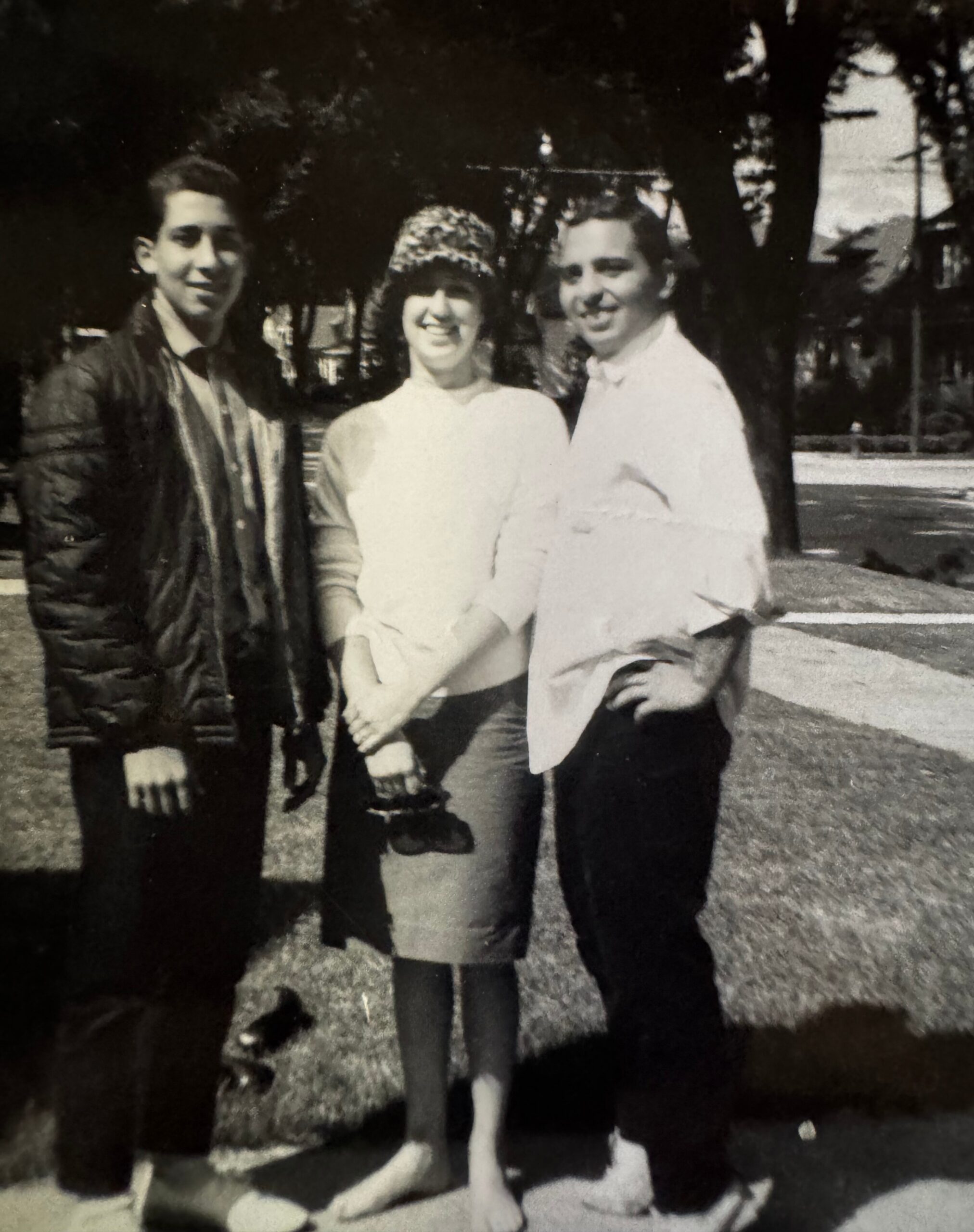 Three friends posing outdoors, smiling, with a woman in a white blouse and furry hat flanked by two men.