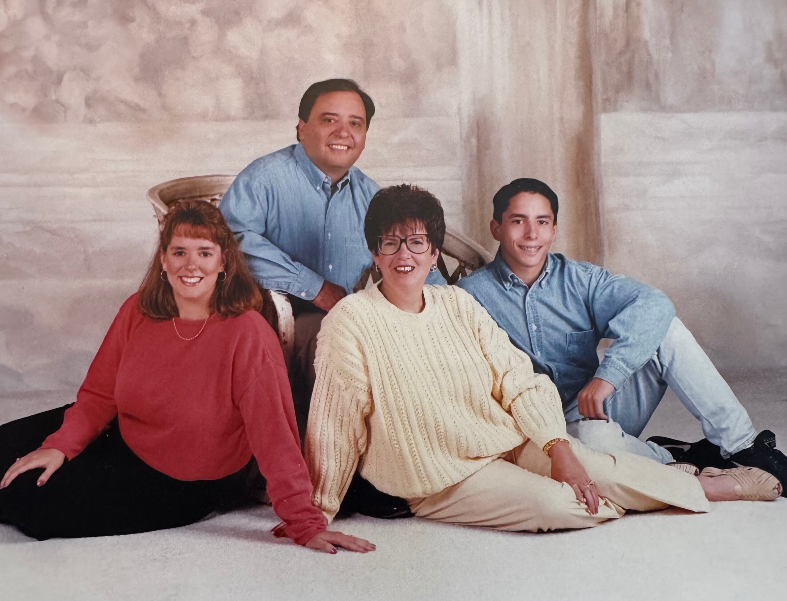 Group photo of four people posed closely together, smiling, wearing casual sweaters and denim against a light backdrop.