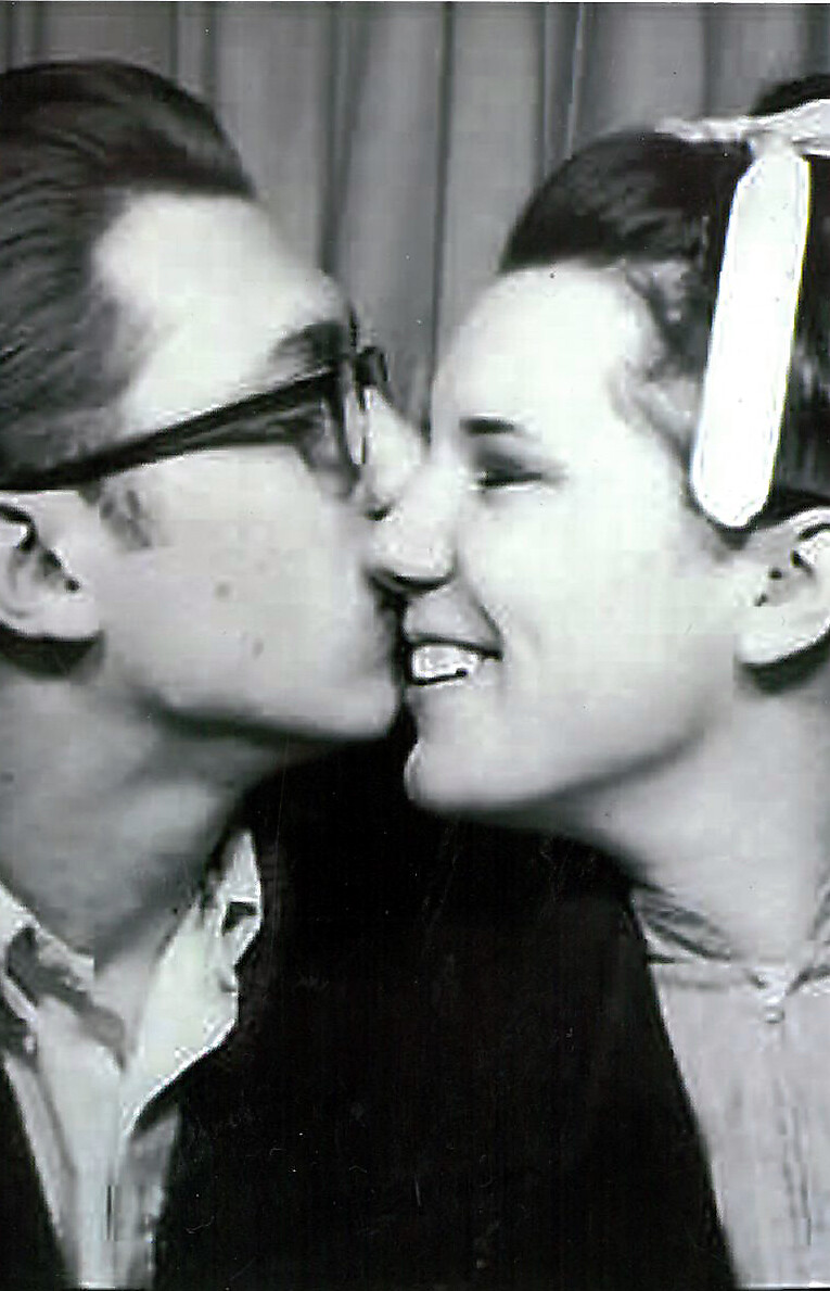 Two people kissing in a close-up shot, with one wearing dark glasses and the other wearing a light-colored headband or ribbon in her hair.