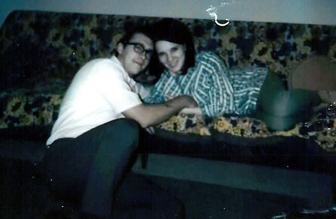 Two people cuddling on a floral sofa, smiling at the camera.