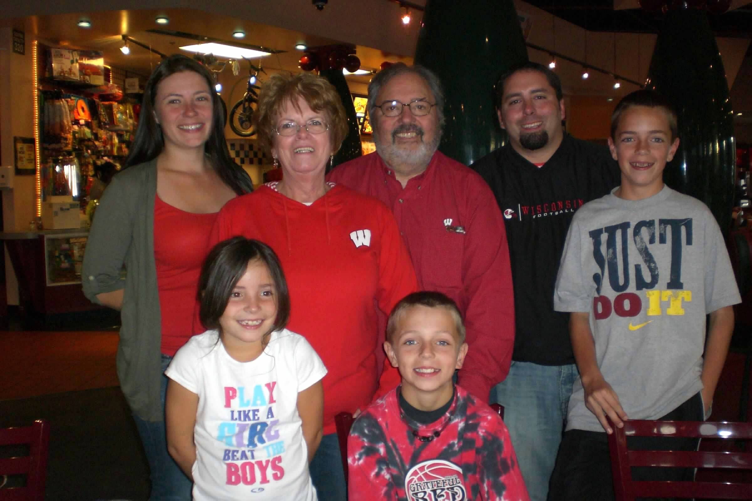 Seven people posing together for a group photo in an indoor arcade or entertainment venue, smiling at the camera.