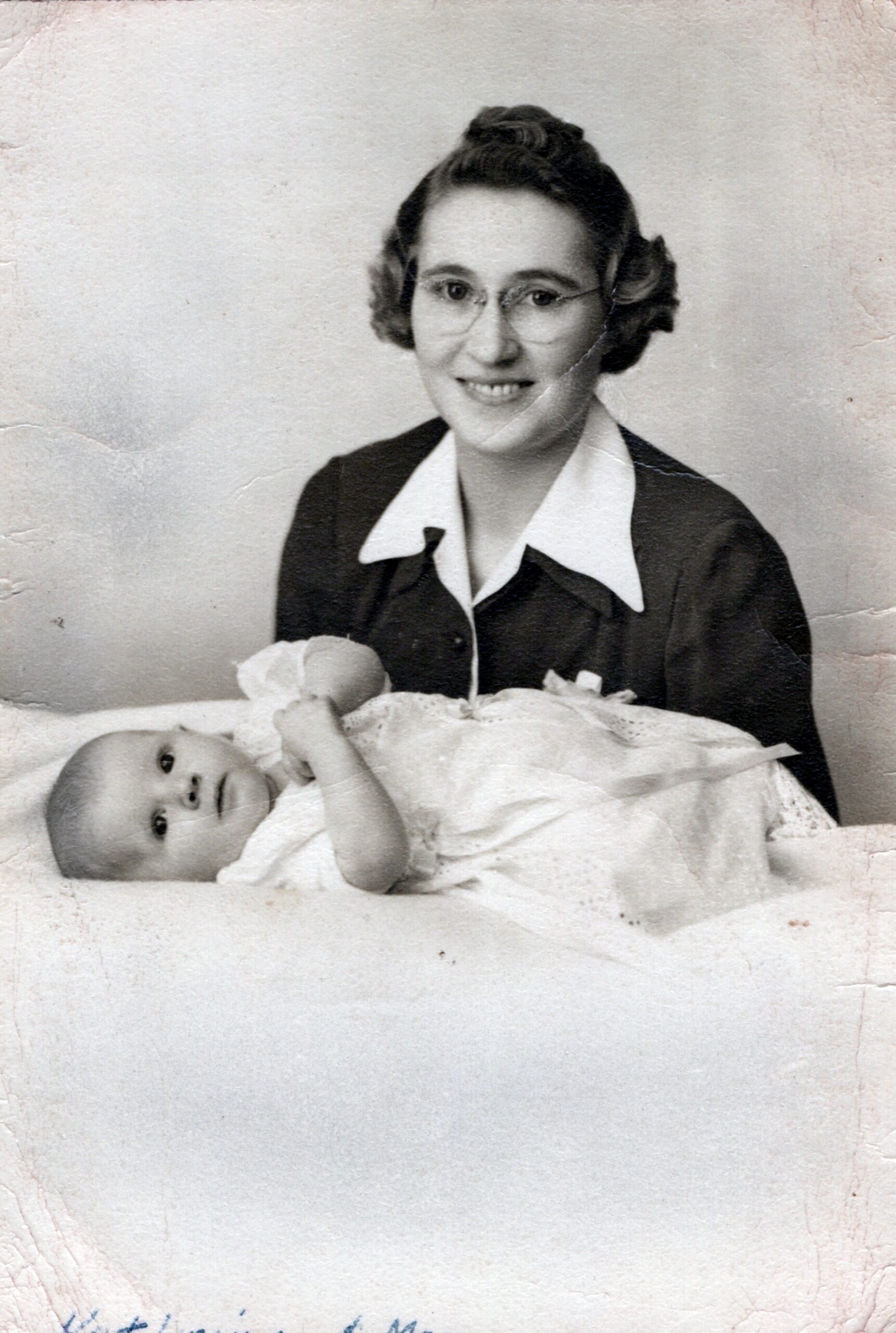 Black-and-white portrait of a smiling woman with glasses holding a swaddled newborn baby.