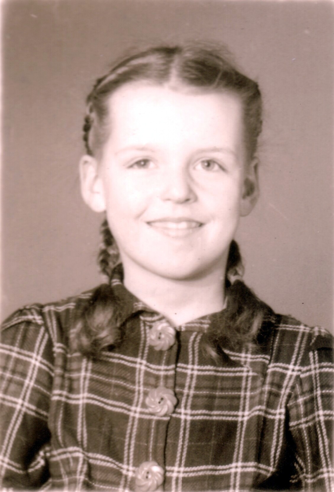 Young girl with braided hair wearing a plaid button-up dress, smiling for a portrait.
