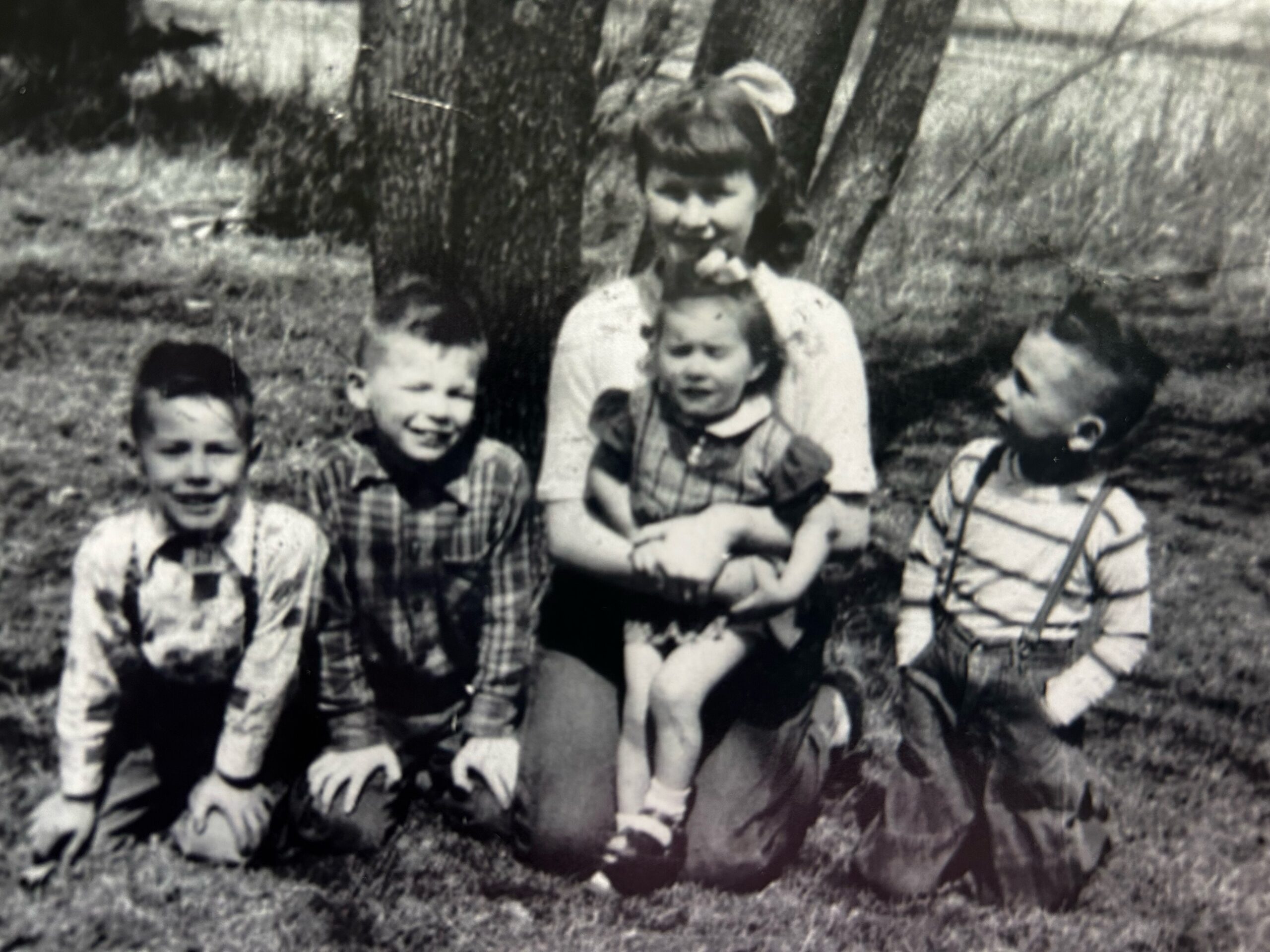 Black-and-white family photo: a mother with a baby and several children outdoors in a yard near trees.
