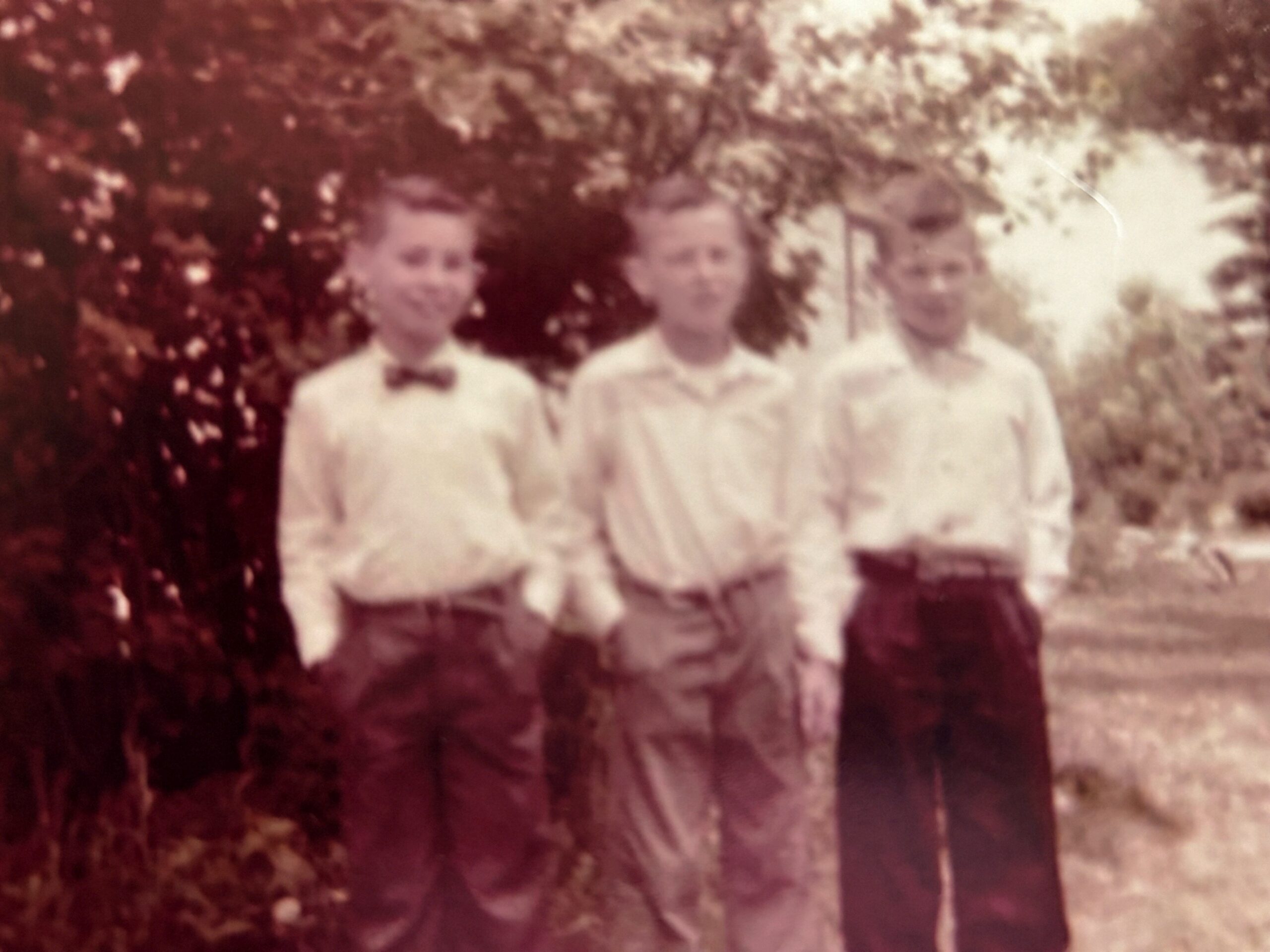 Three women stand together outdoors in light dresses, in a vintage sepia-toned photo.