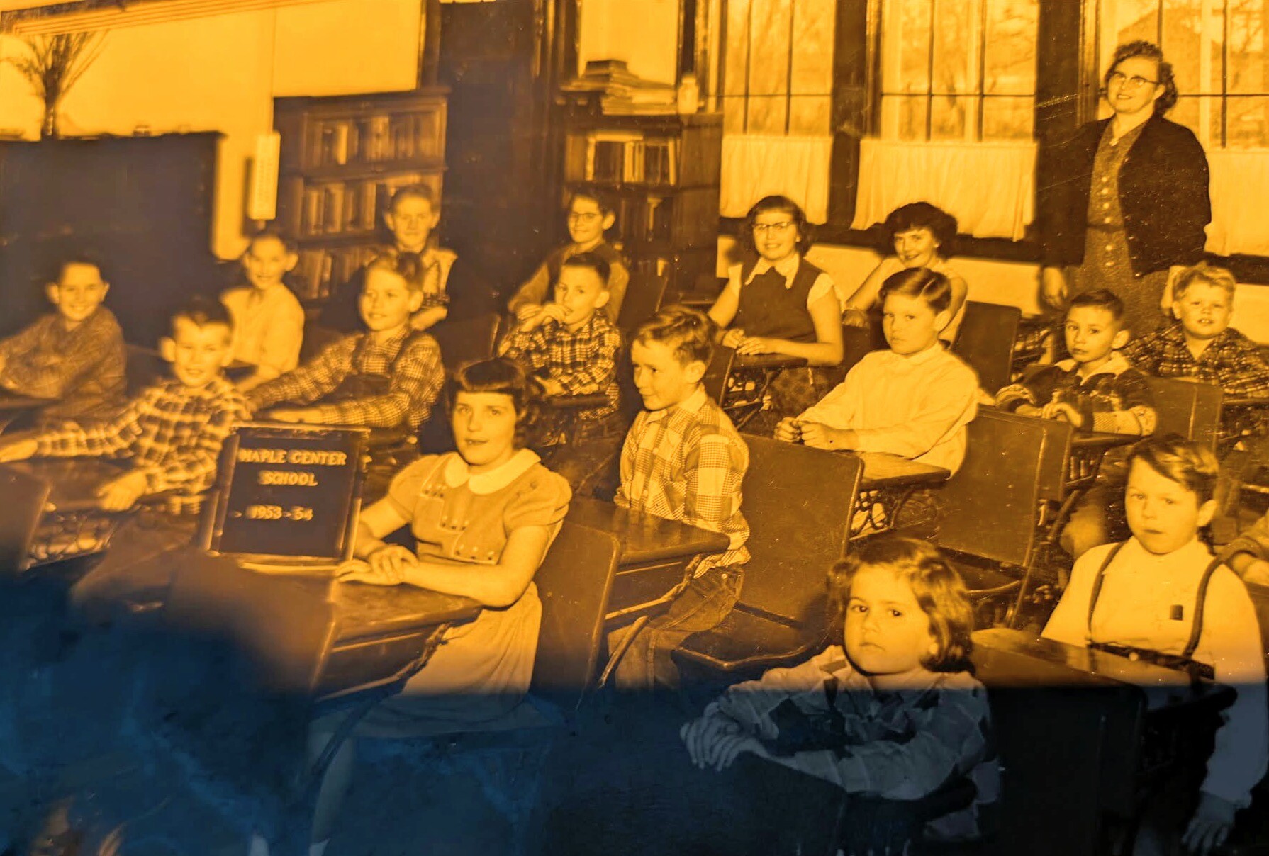 Group of elementary students in a 1950s classroom posing for a photo; Maple Center School 1953–54 sign visible in the foregrounds.