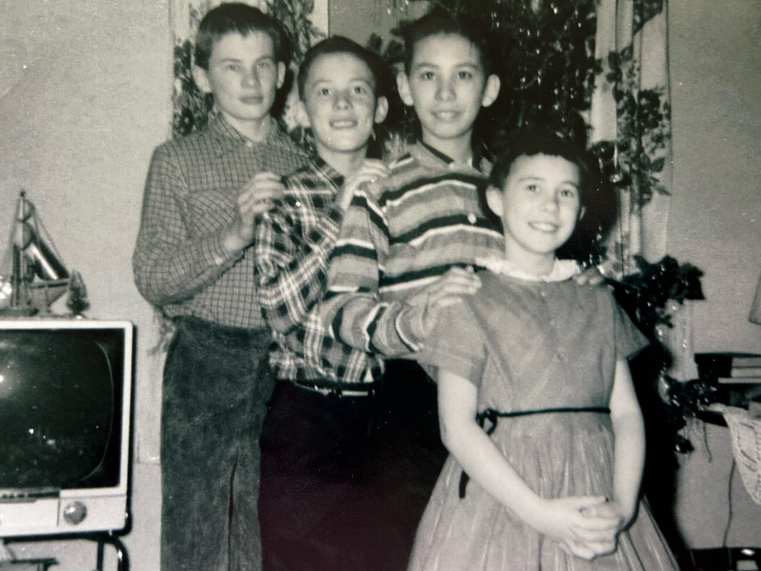 Two adults and two children pose indoors around a birthday cake, smiling in a black-and-white photo.