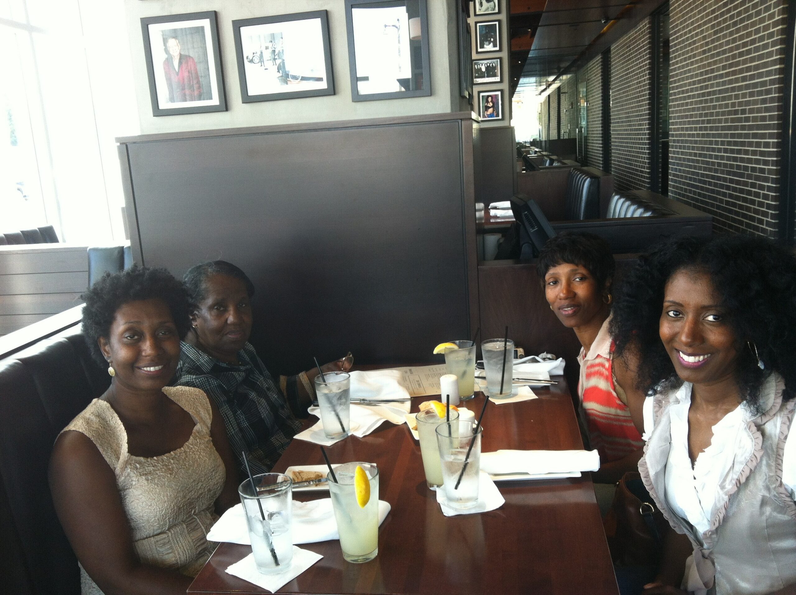 Five women smiling at a restaurant table with tall glasses of lemonade and lemon wedges, seated in a booth.
