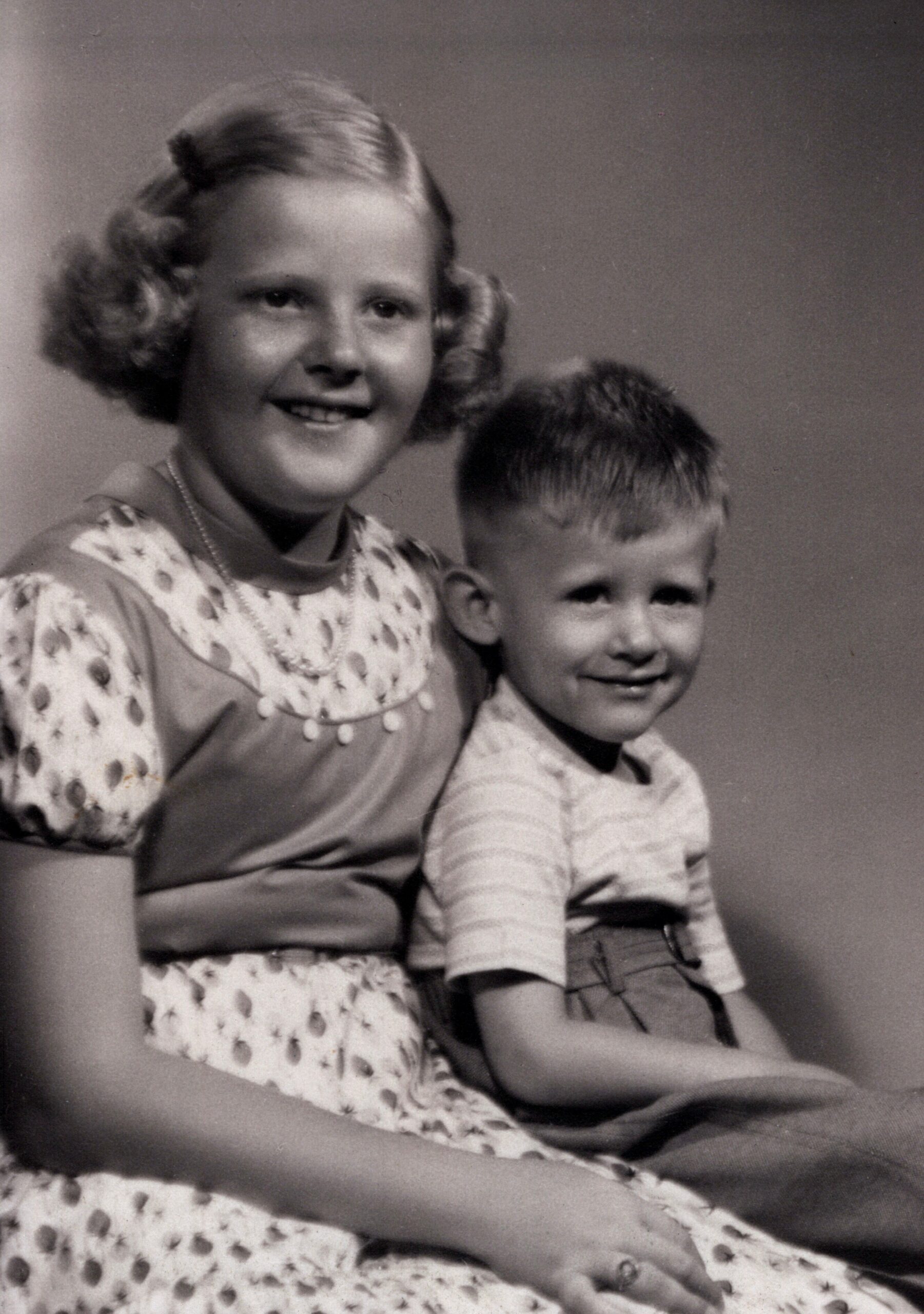 Smiling woman with short curled hair seated beside a young boy in a vintage studio portrait (black and white).