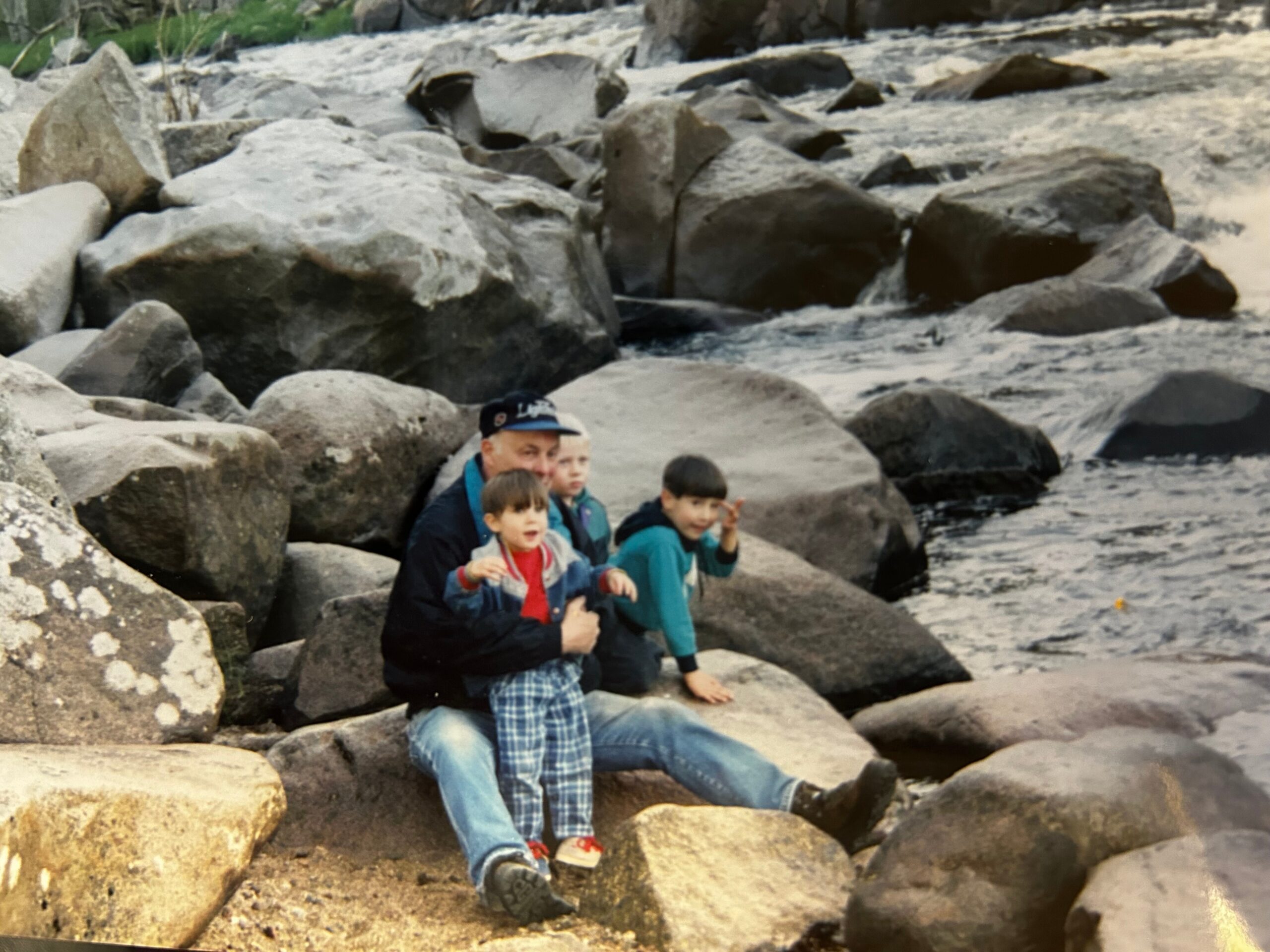 Group of people sitting on large rocks along a rocky shoreline by the water.