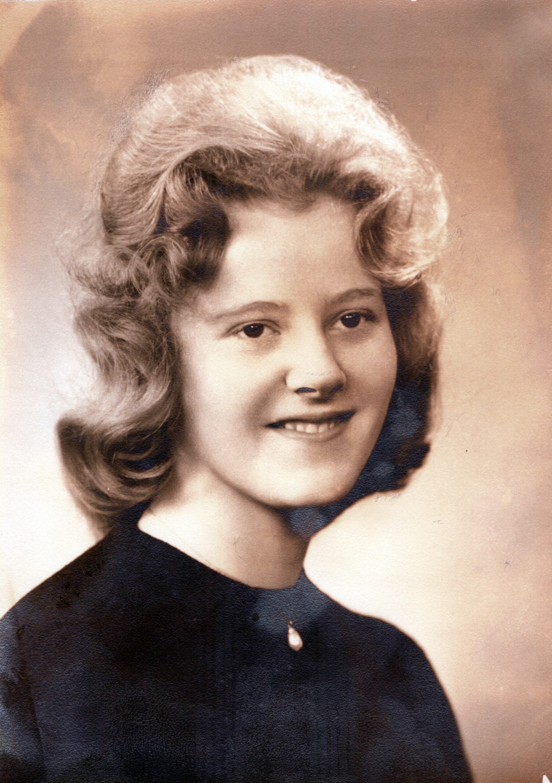 Smiling young woman with voluminous blond hair in a vintage portrait.