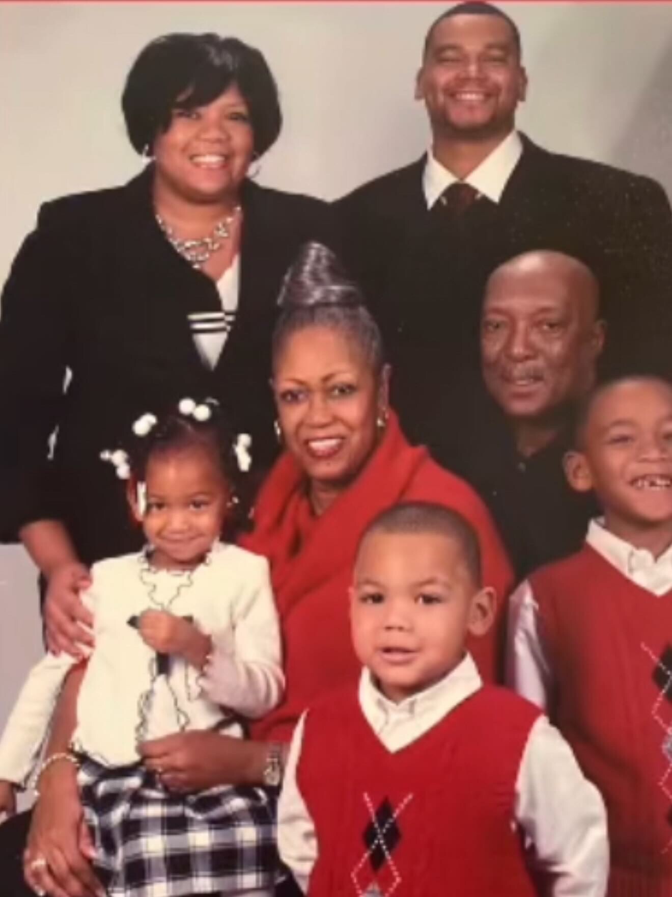 Smiling family portrait with four children and two adults in formal attire, posing together indoors.